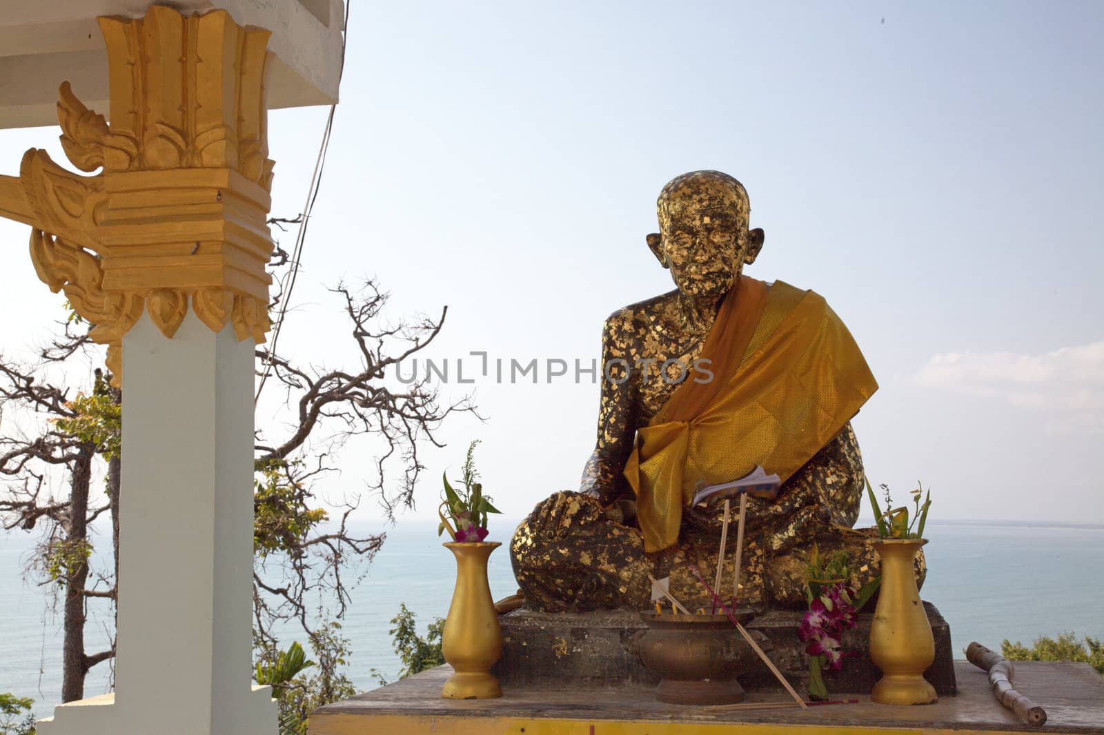 seated golden Buddha with offerings in front off the sea - vertical
