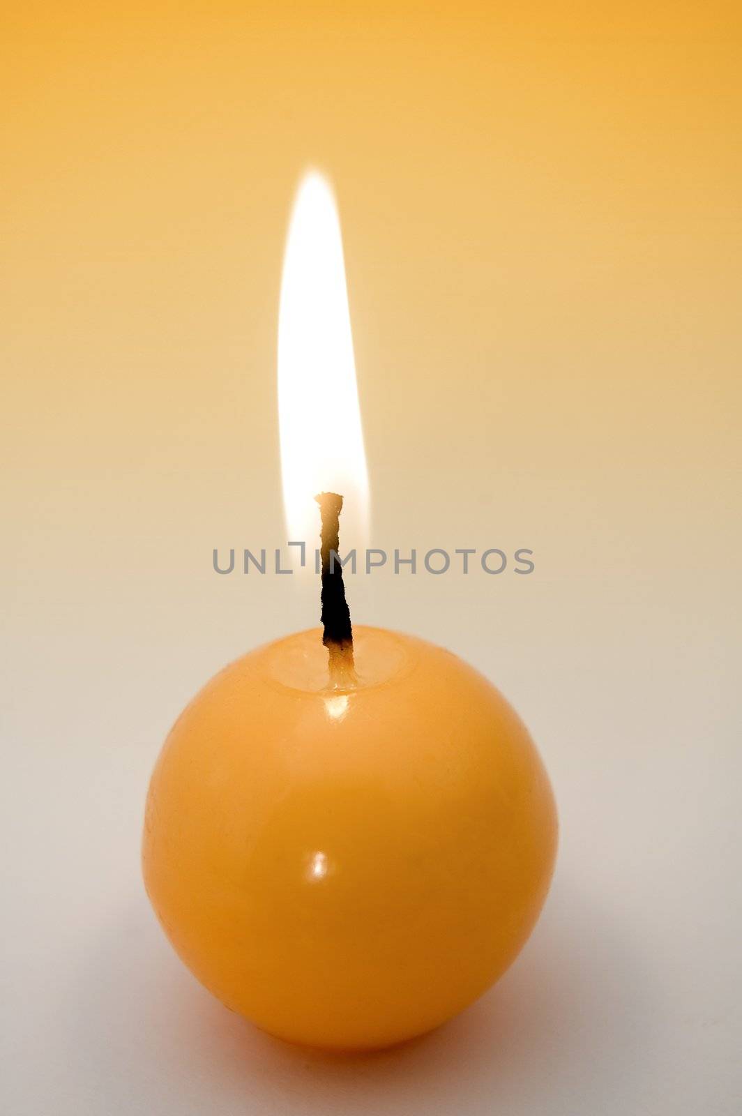 small yellow burning candle, yellow to grey background