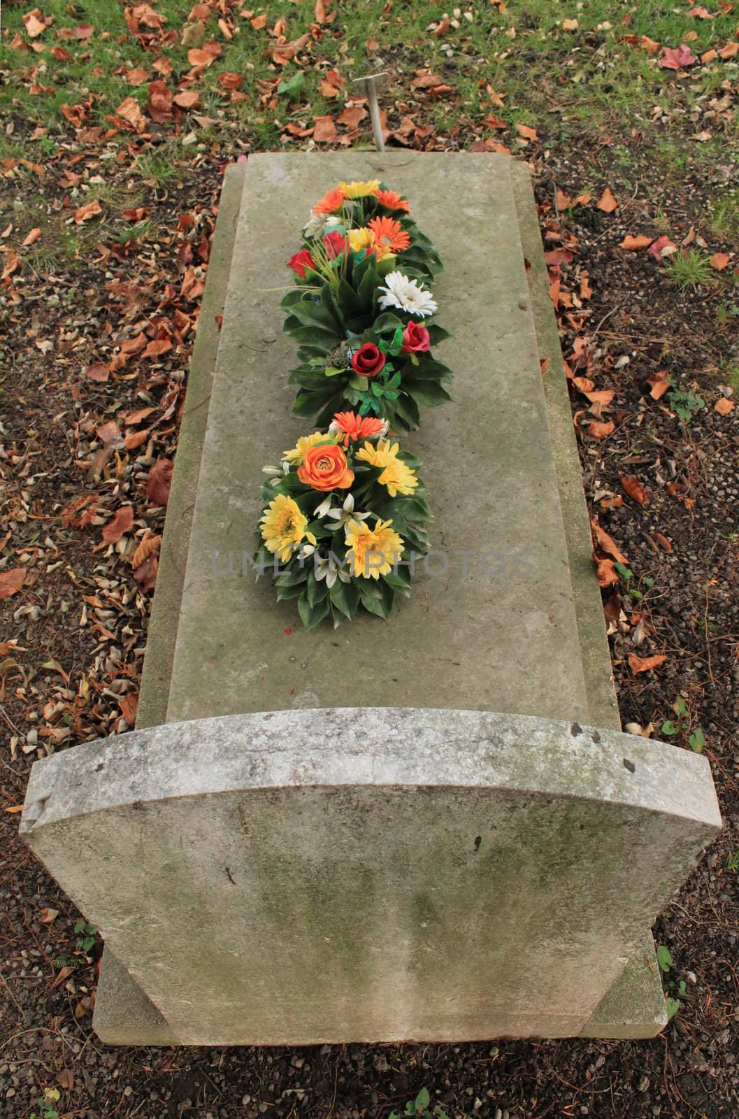 Tombstone covered with beautiful colored flowers by autumn weather with red leaves on the ground