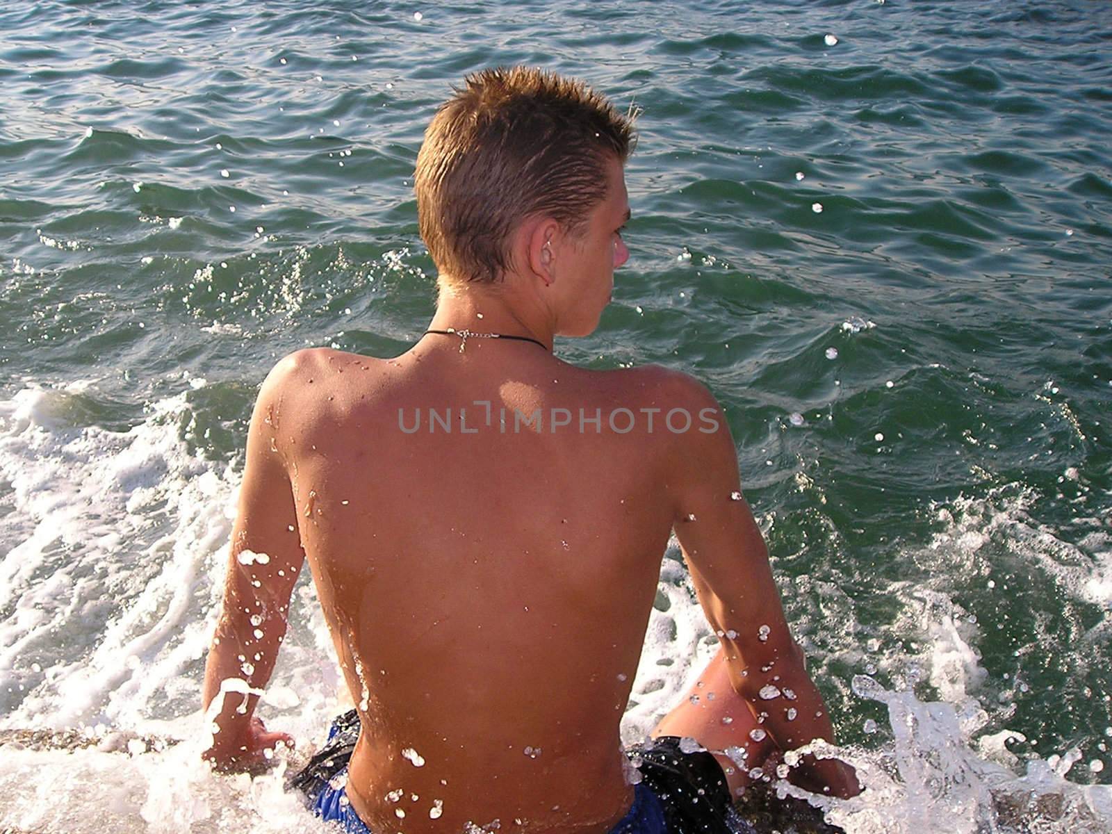 youth sits in summer on the shore sea and drops of waves pour over by his coolness.