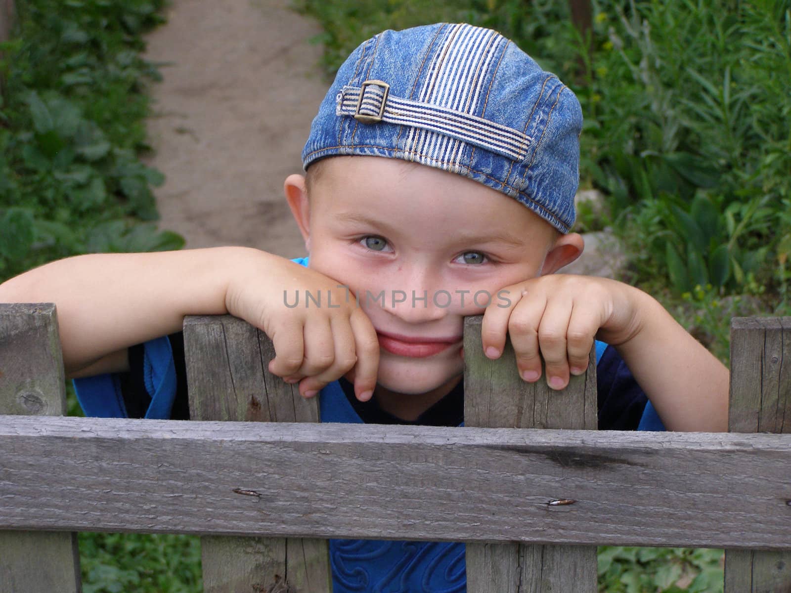 Little boy leaned against the fence. It seems that he awaits something, fixedly looking into your eyes.