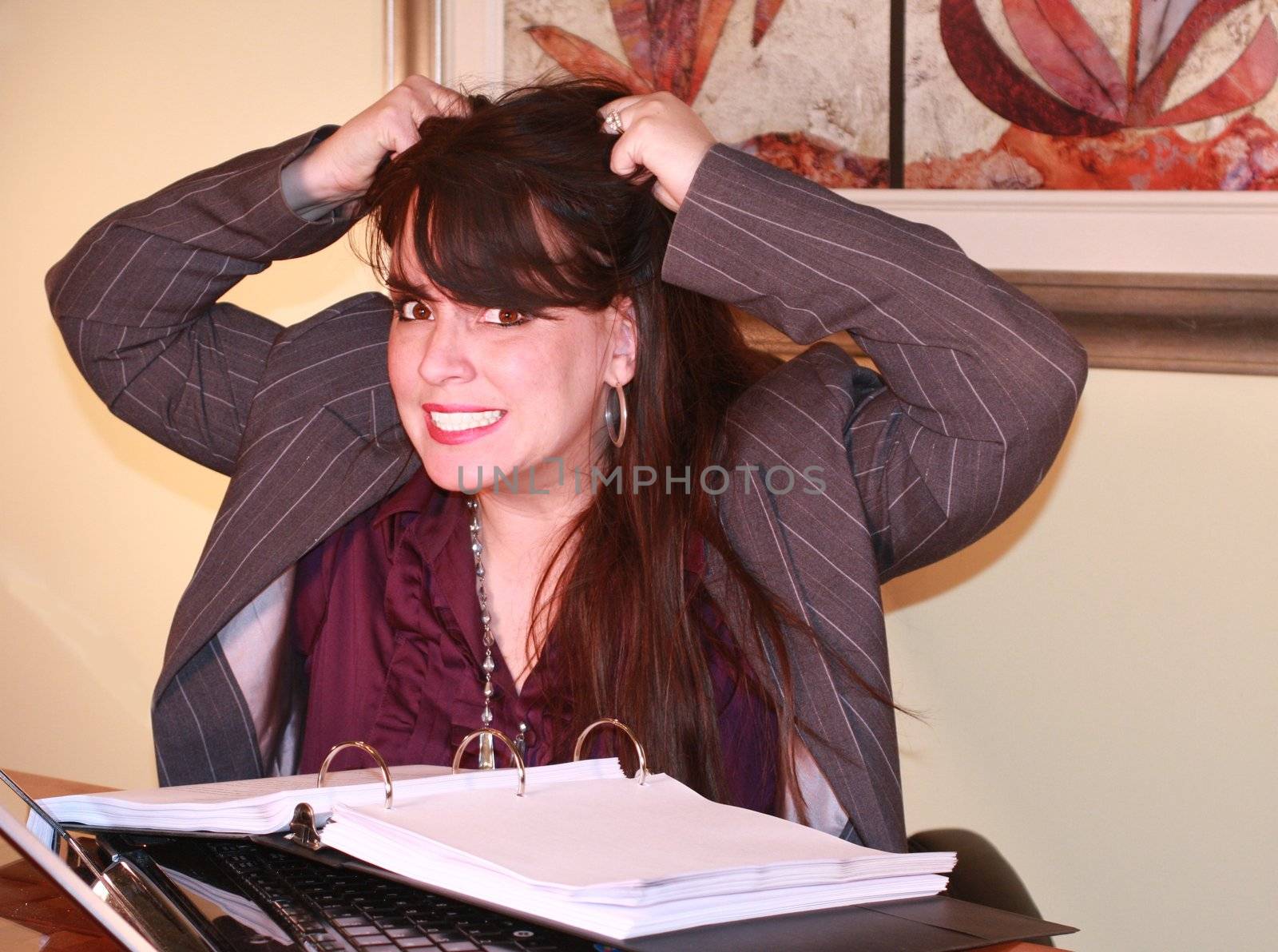 Attractive business woman in office sitting at desk. Computer in the foreground and executive wall art in the background.