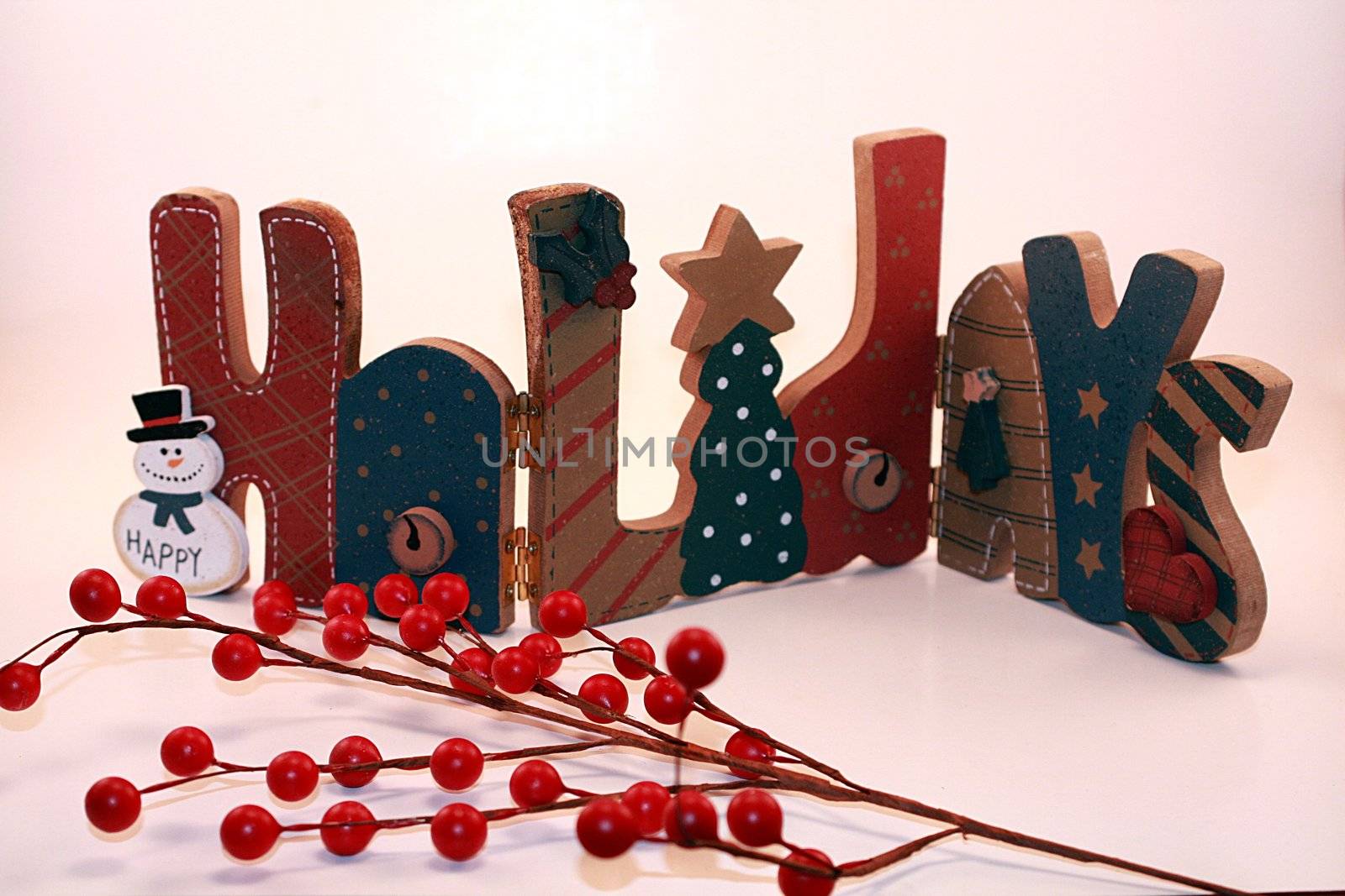 Wooden holidays sign with red holly berries in foreground. Christmas decoration is set against a white background.
