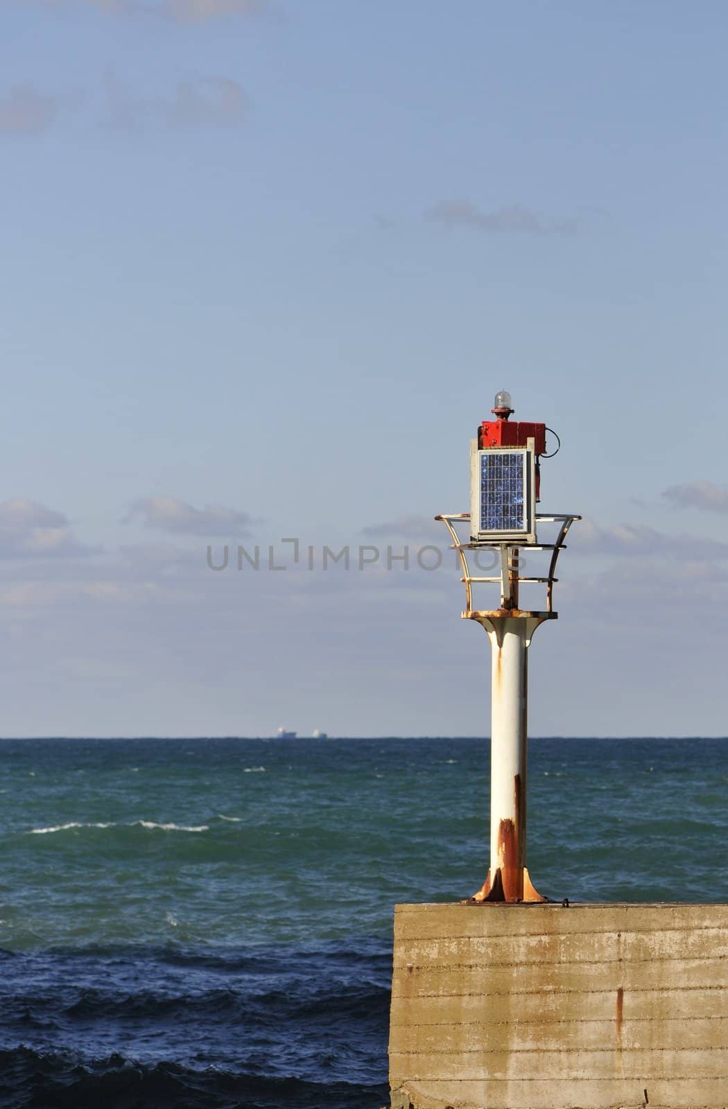 Little solar lighthouse on a concrete jetty with sea and sky in the background