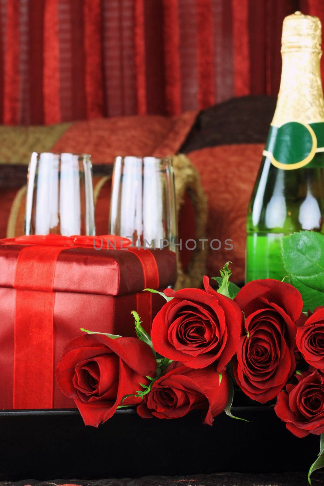 Beautiful long stem red roses with gift, wine and glasses in a breakfast tray on a bed.