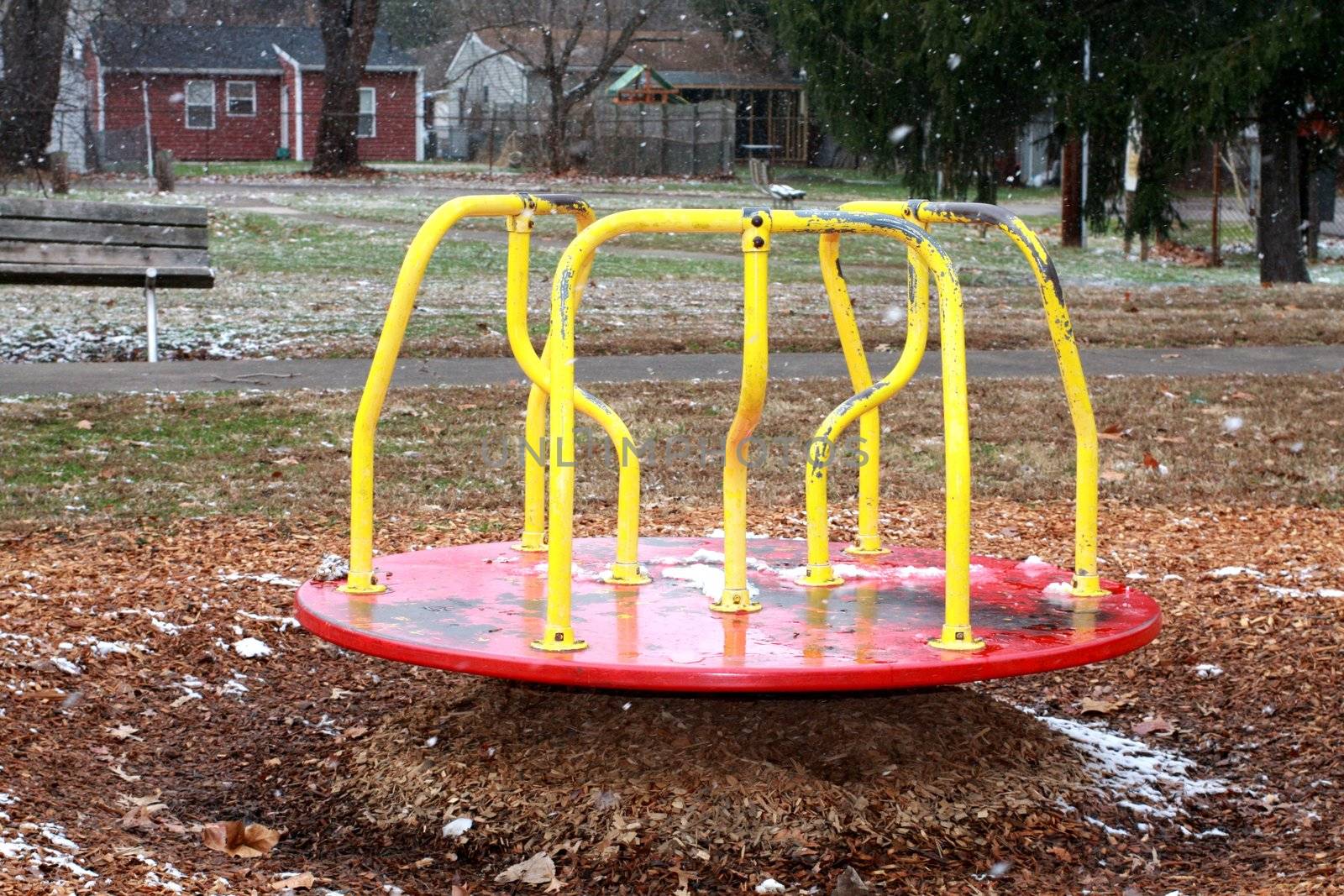 Merry go round in park during winter weather. Snowing in background of park. Isolated merry go round with park bench in background.