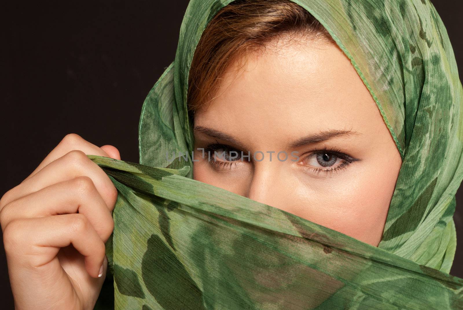 Young arab woman with veil showing her eyes on dark gray background by dgmata