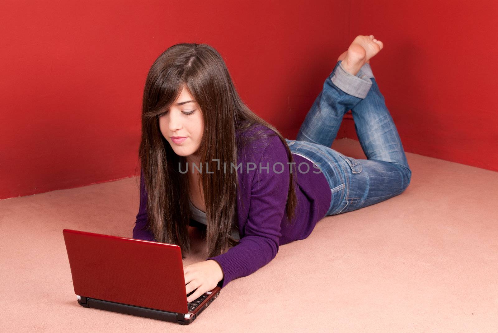 Young woman with laptop lying on floor at home by dgmata