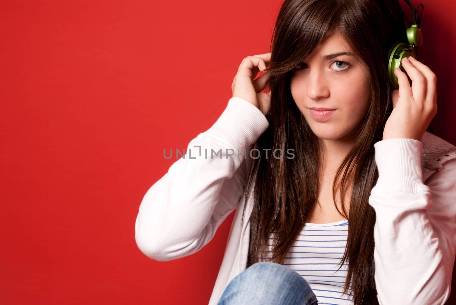 Young girl listening music with headphones on a red wall