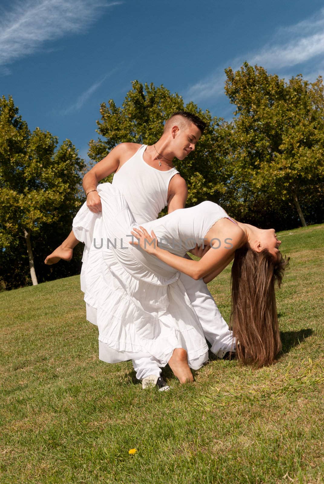 Young beautiful couple dance and embrace on grass over sky