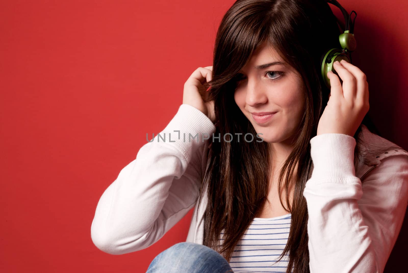 Young girl listening music with headphones on a red wall by dgmata