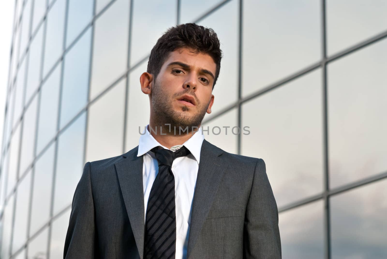 Young businessman looking to camera on modern building background