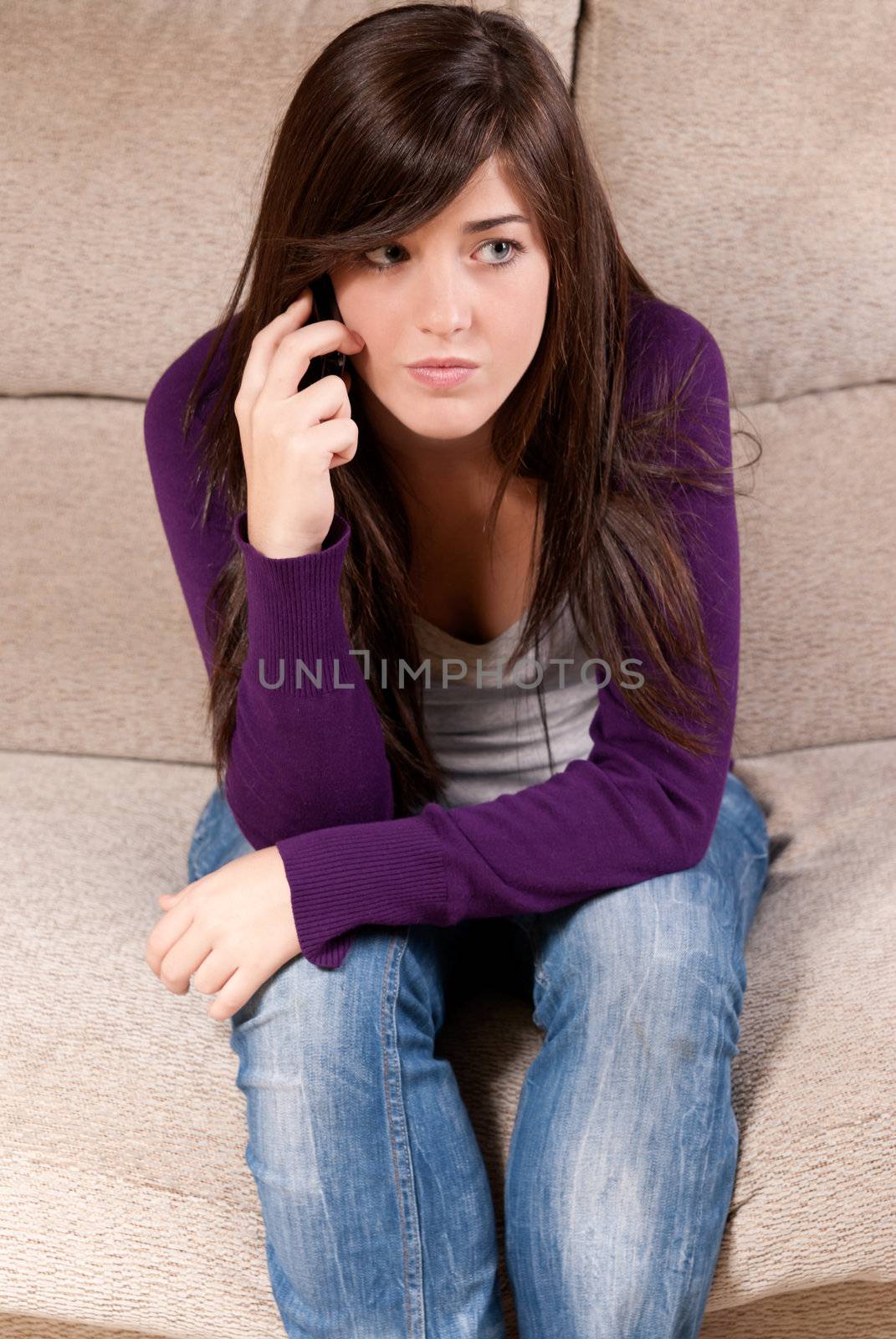 Young girl concerned talking by telephone bad news sitting on sofa by dgmata