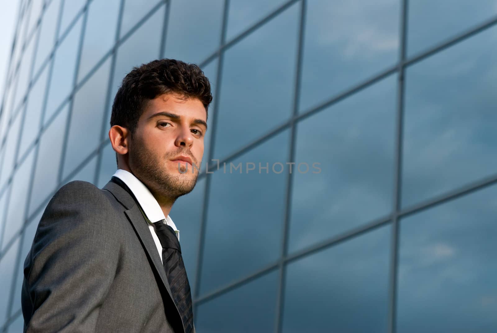 Young businessman looking to camera on modern building background