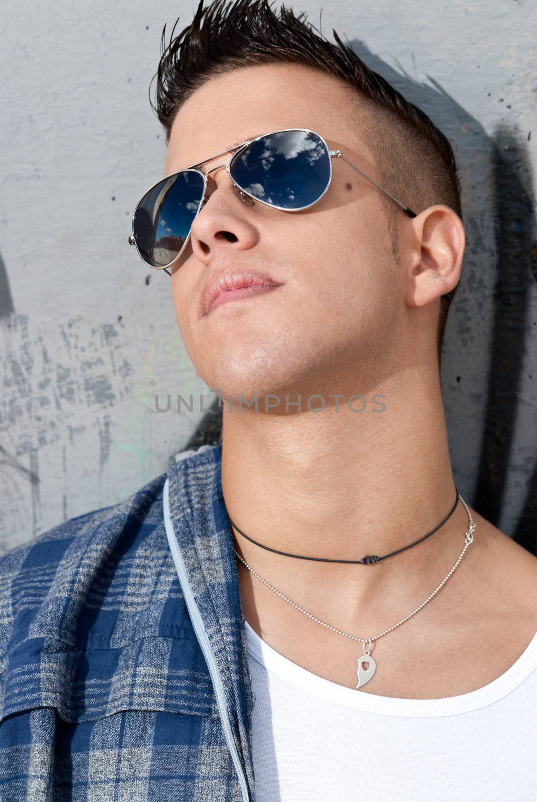 young male urban fashion sky on sunglasses over wall