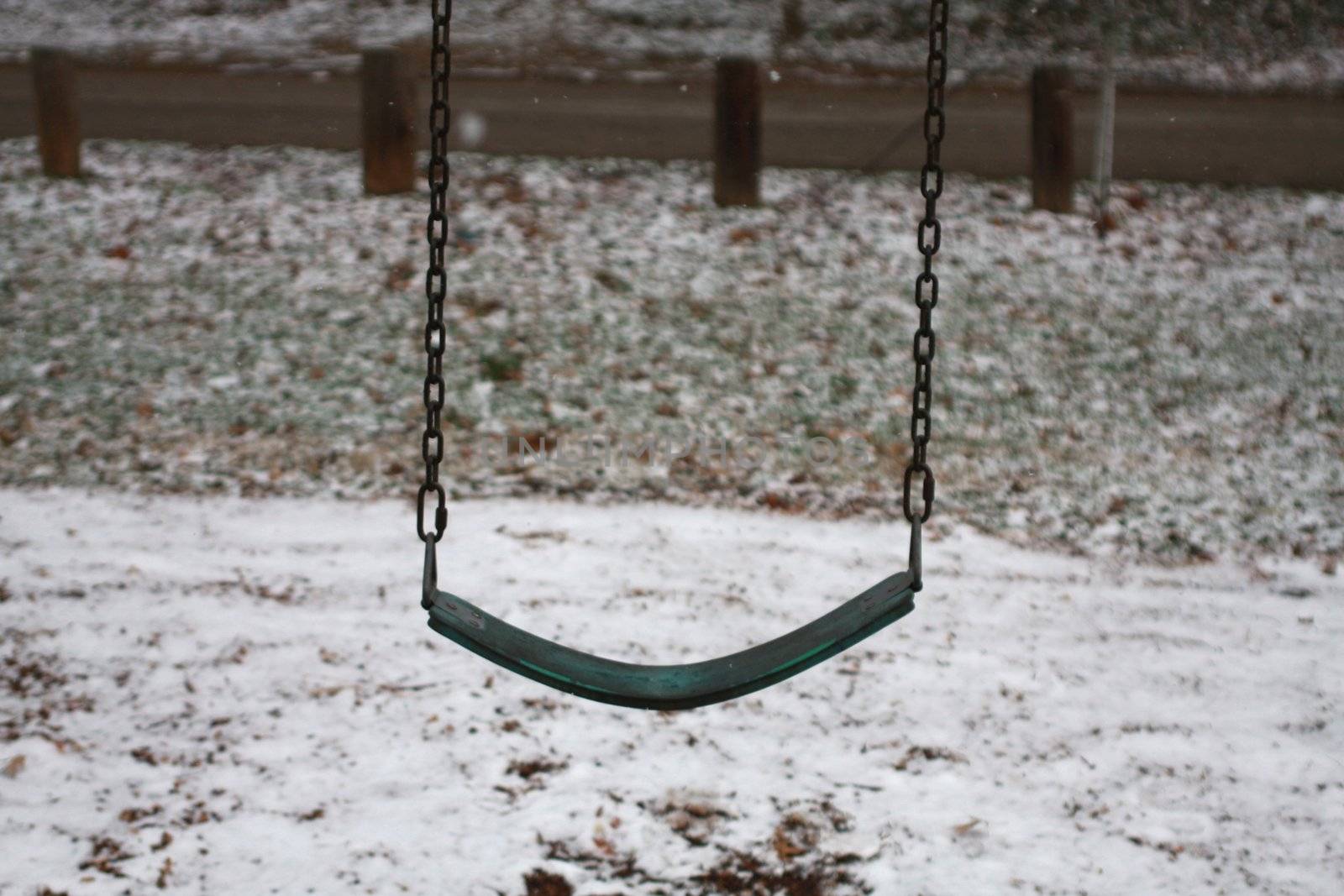 Isolated park swing outdoors for winter season. Snow background behind playground swing.
