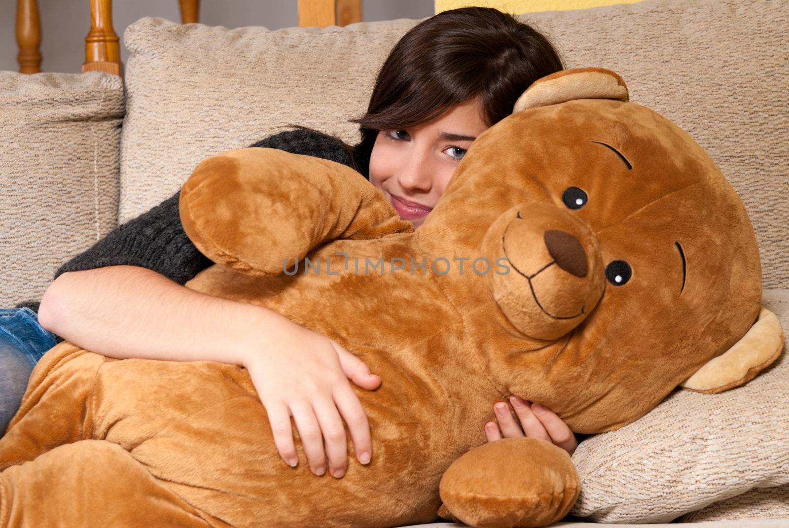 Young woman embracing teddy bear lying on on sofa