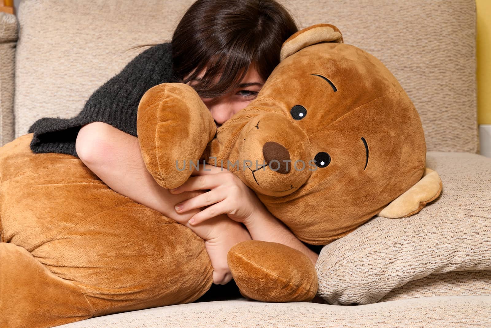 Young woman embracing teddy bear lying on on sofa close-up by dgmata