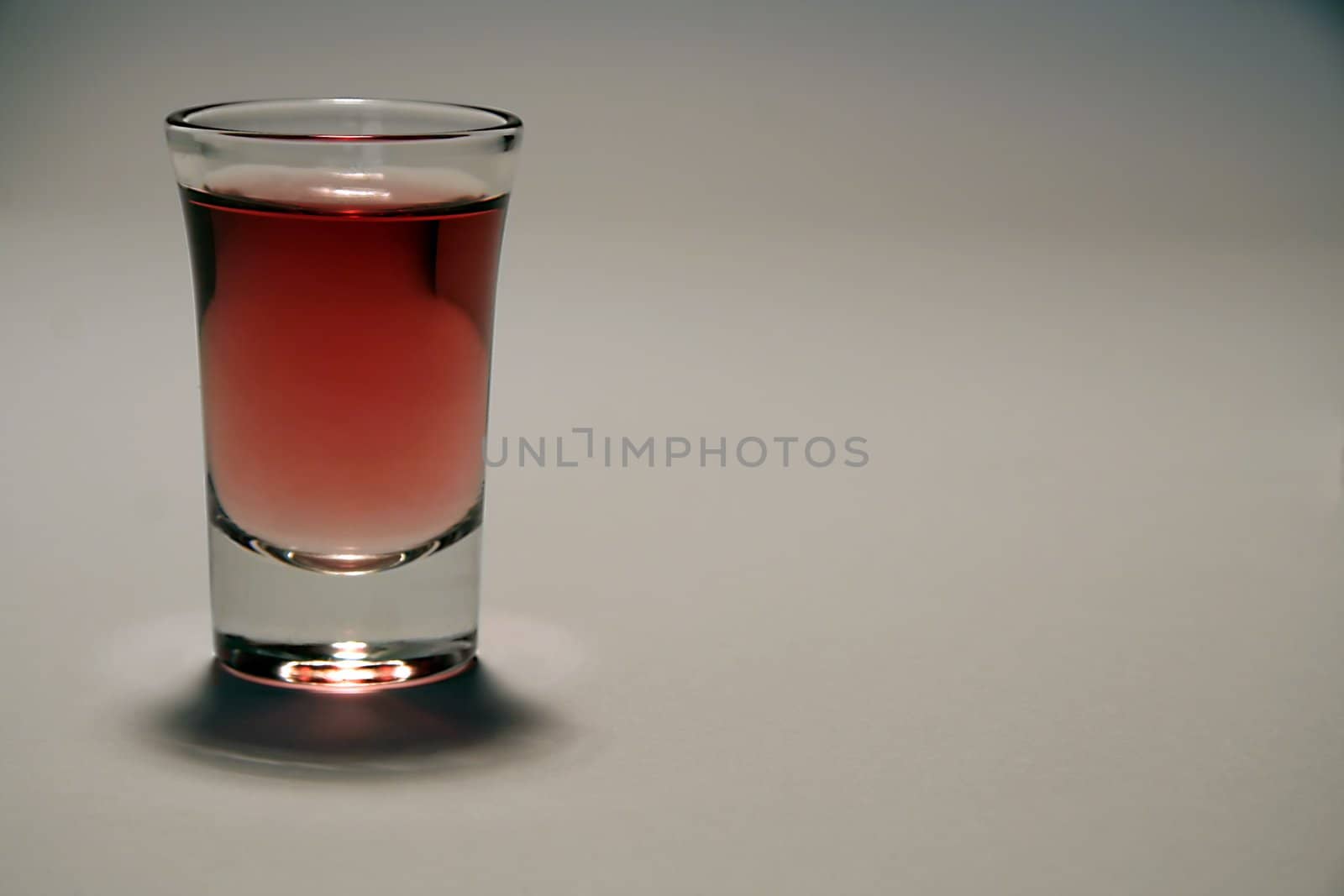 small glass of red alcohol, grey background