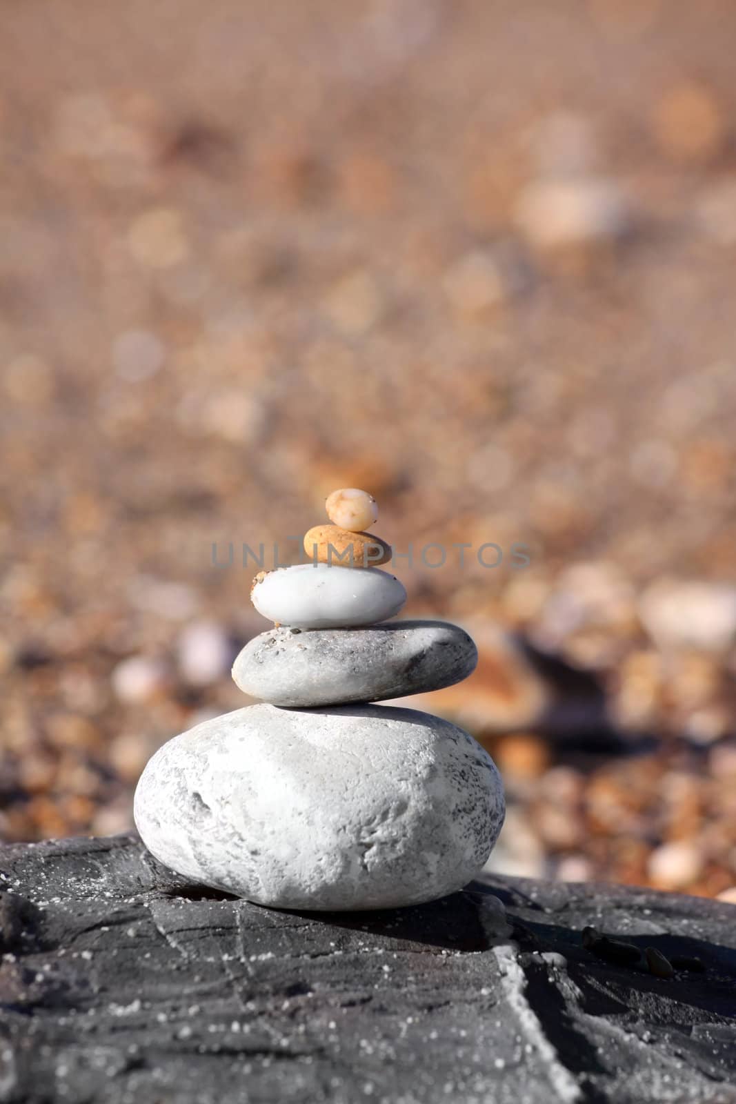 A pile of beach pebbles stacked on top of each other set on a rock. A soft focus pebbled beach set to the background.