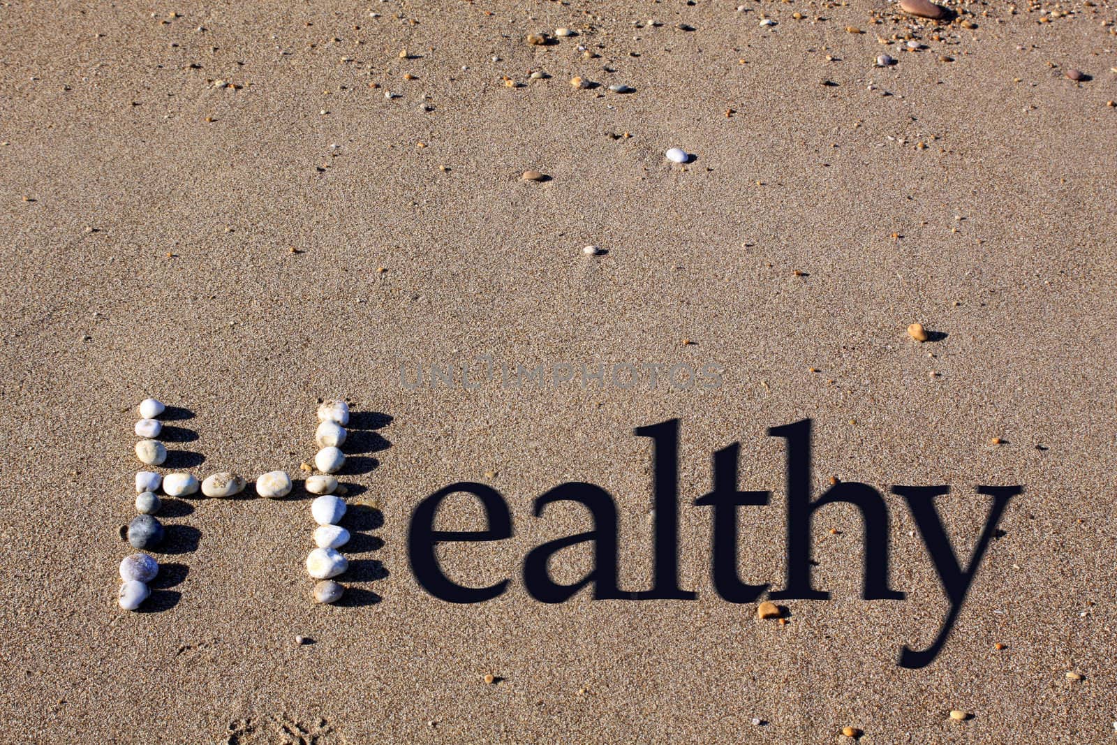 An upper cased letter 'H' formed by beach pebbles on the sand. The word healthy is spelt out by the addition of shadowed text.