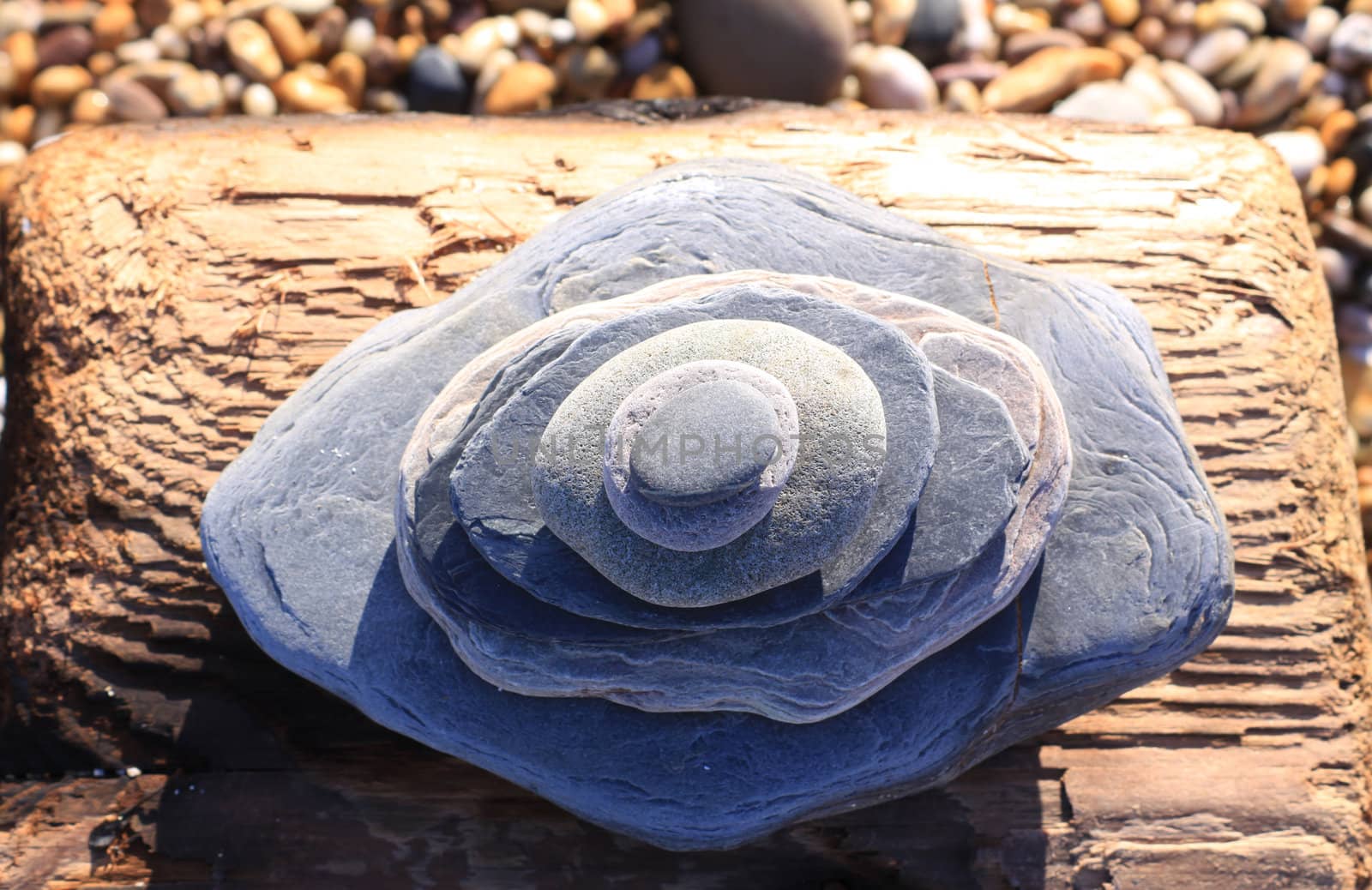 A stack of pieces of slate piled on top of each other in various sizes, set on a block of drift wood. Slate has been shaped by the washing sea.