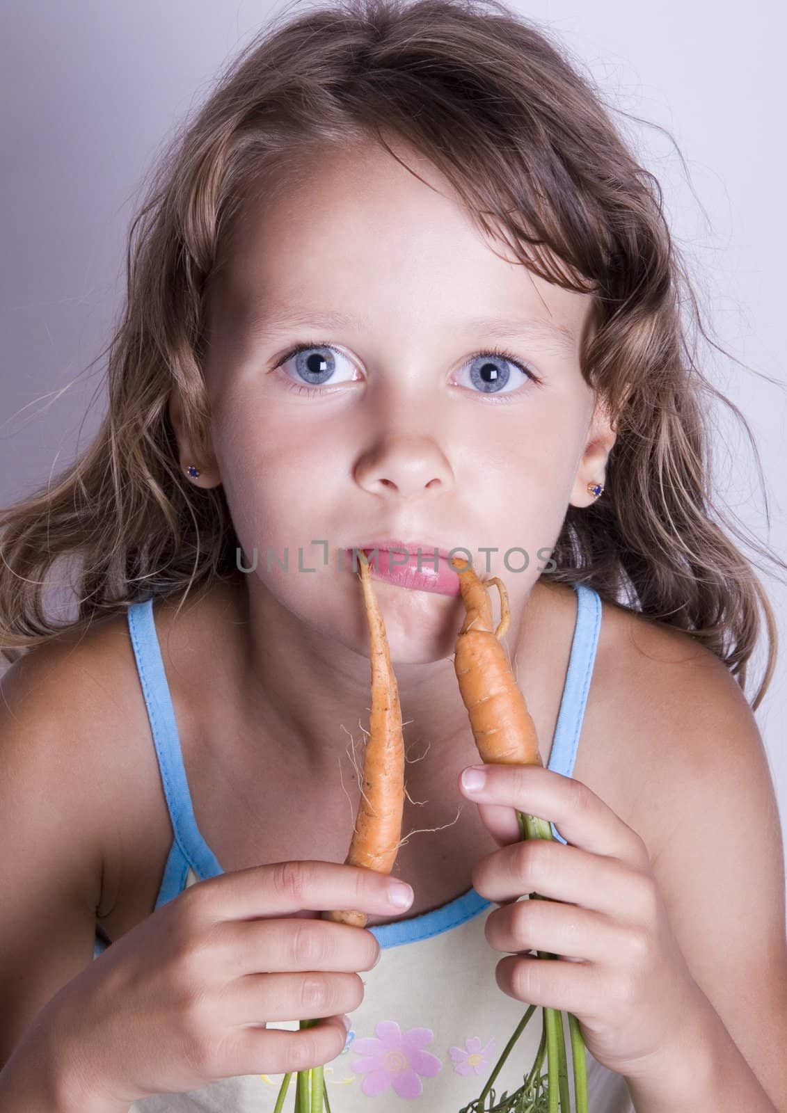 A sweet young girl eating fresh carrot. The child is on a white background