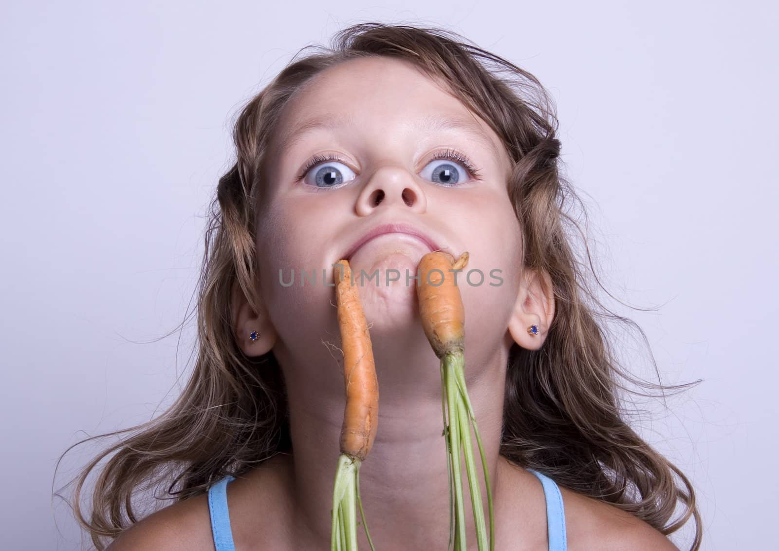 A sweet young girl eating fresh carrot. The child is on a white background