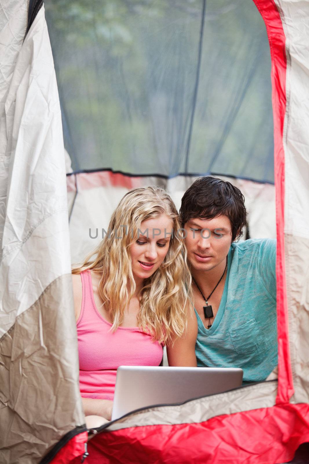 Young couple using laptop in tent while camping