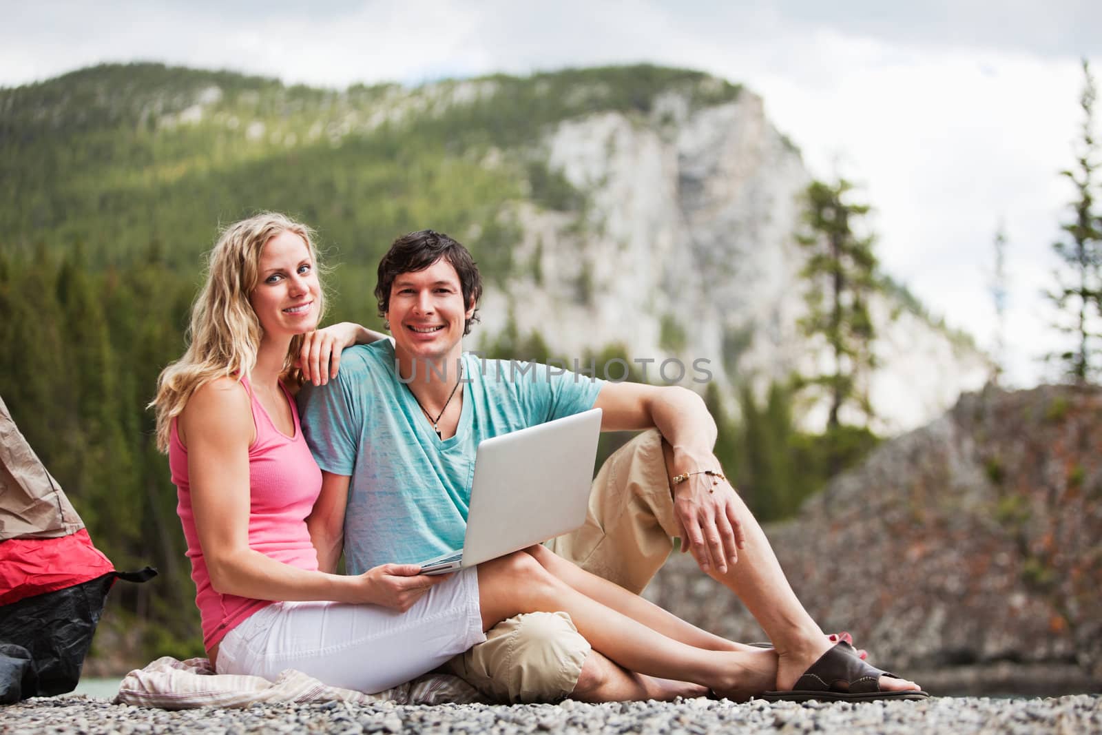 Portrait of happy relaxed young couple with laptop while camping