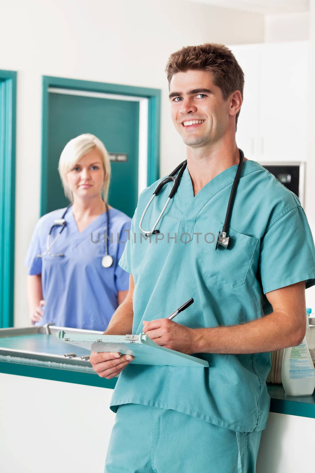 Portrait of smiling male veterinarian with clipboard while assistant in the background