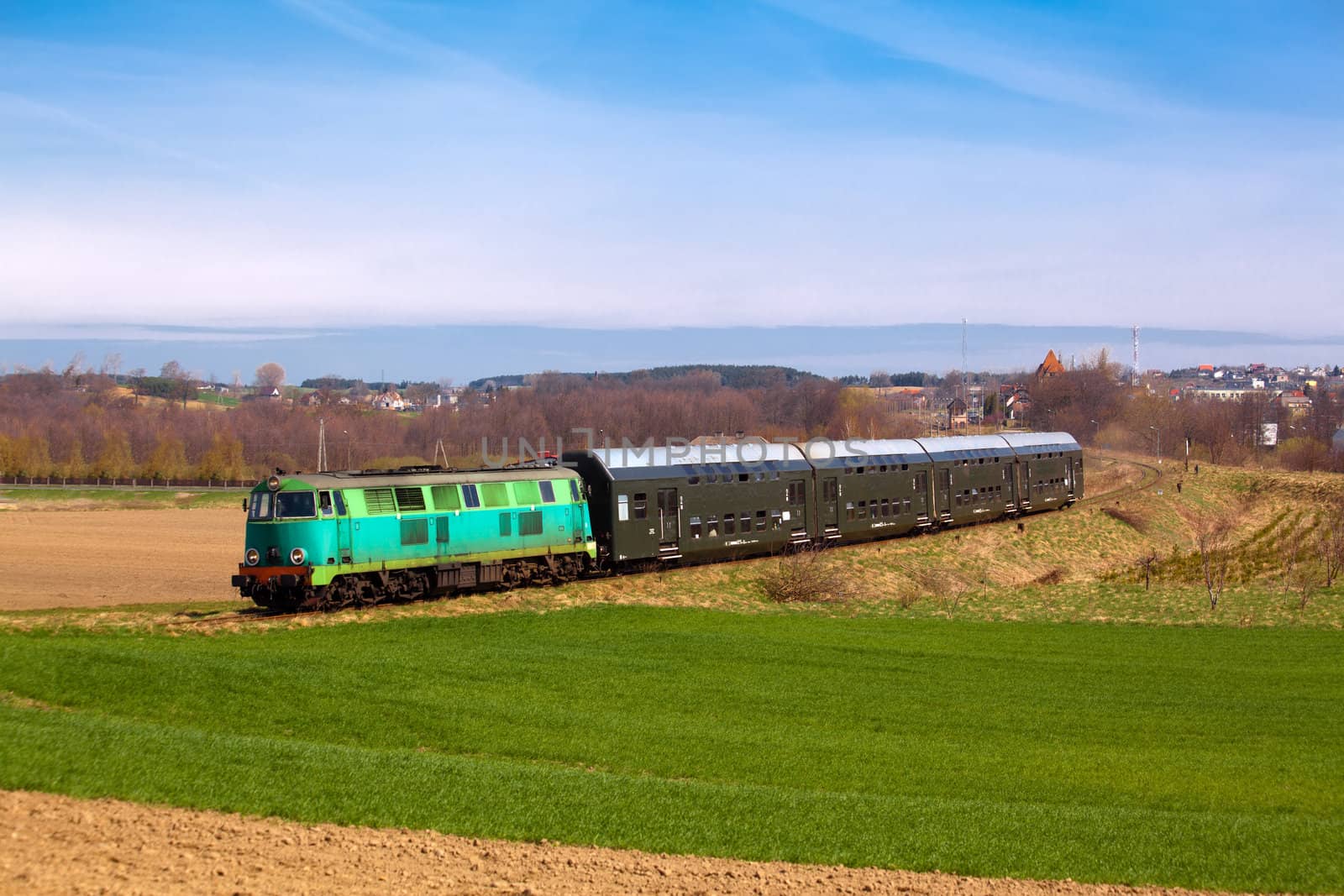 Passenger train hauled by the diesel locomotive passing the sunny landscape
