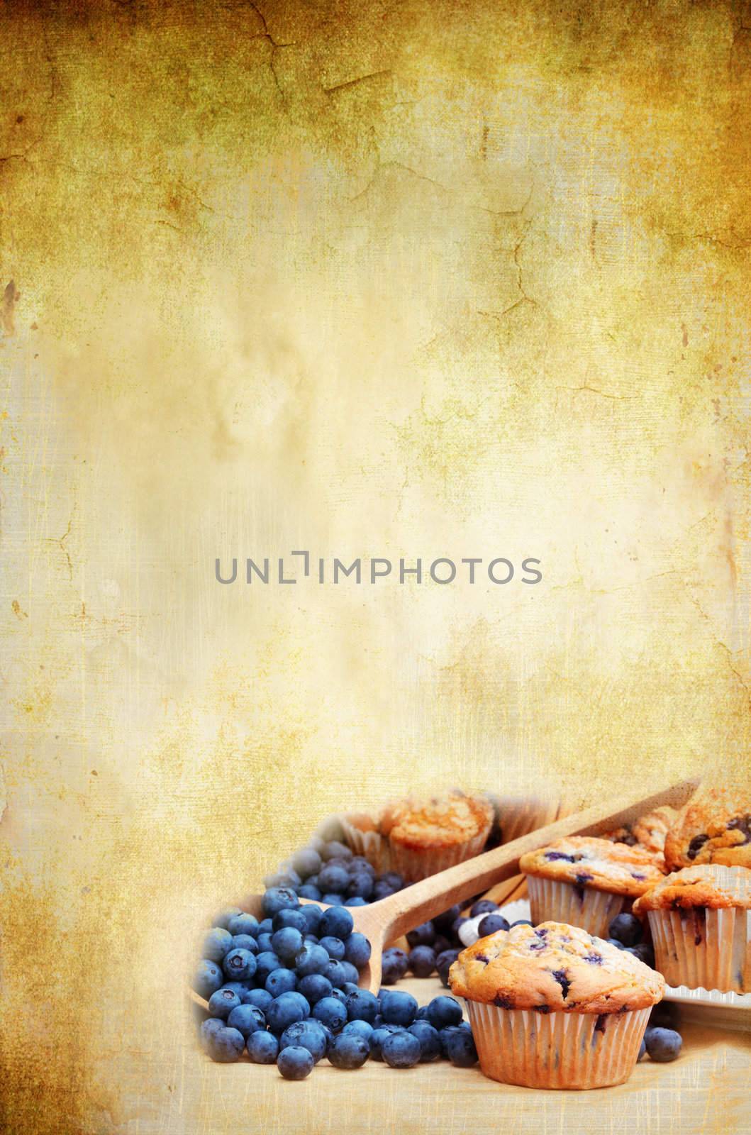 Blank background for recipe with room for copyspace. Blueberry muffins with fresh blueberries spilling from a wooden spoon in lower corner. 