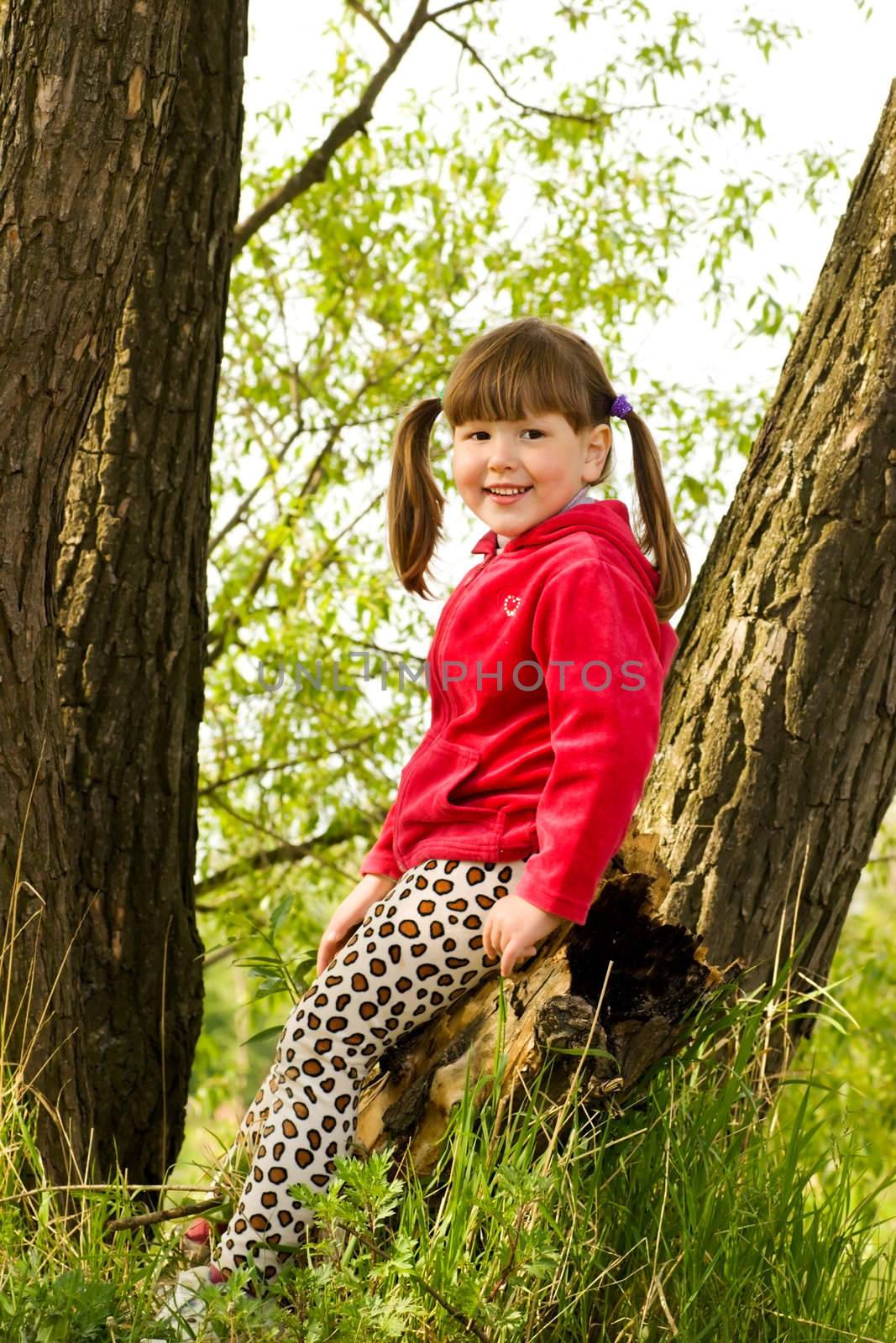 Smiling little girl sitting on tree in forest