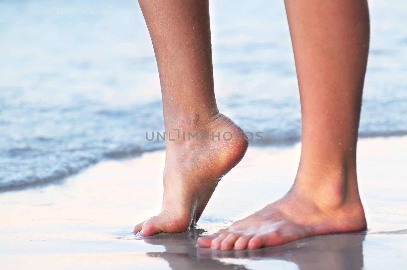 Feet of a young woman touching water on tropical beach