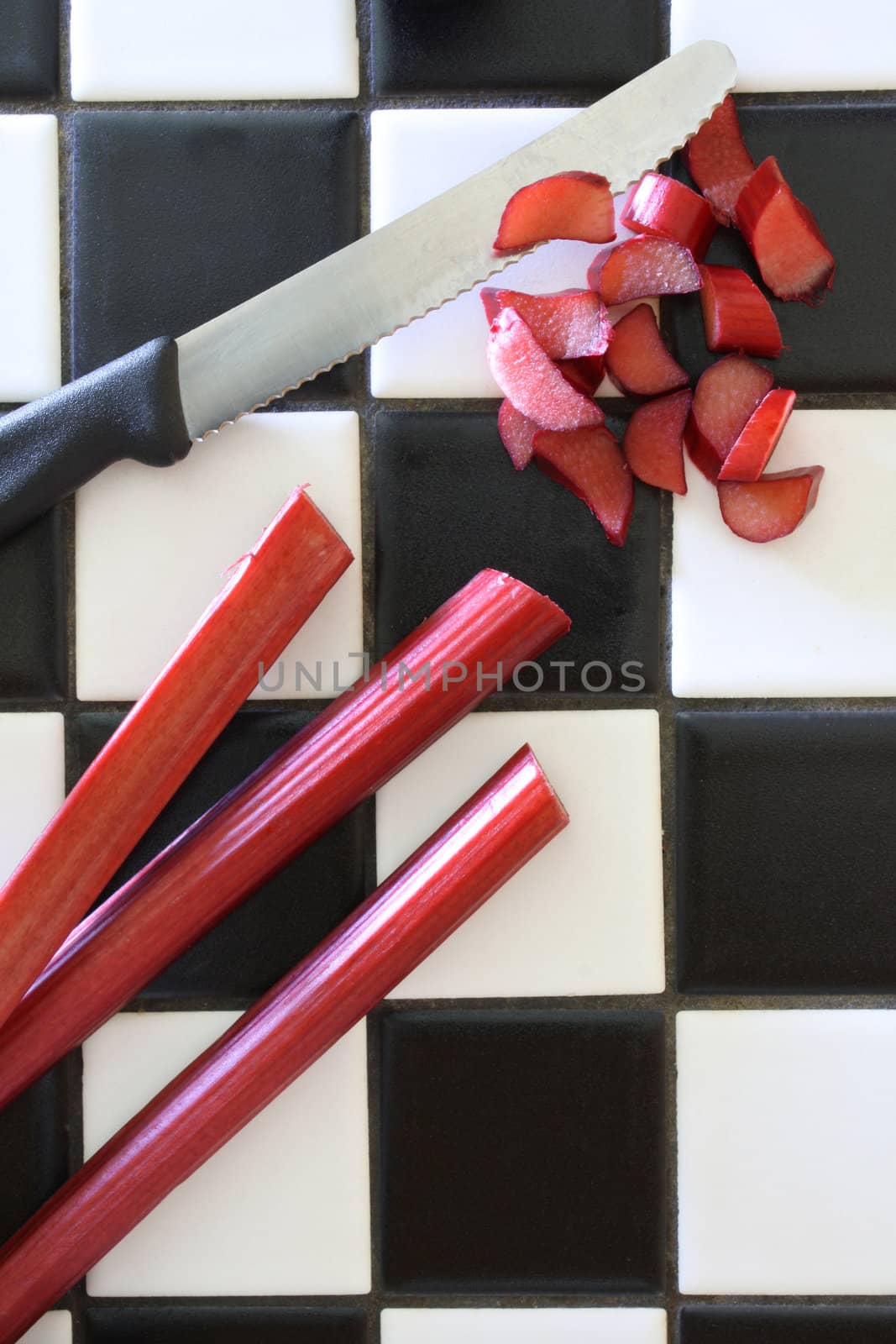 Fresh garden rhubarb, being sliced on a black and white tile counter.
