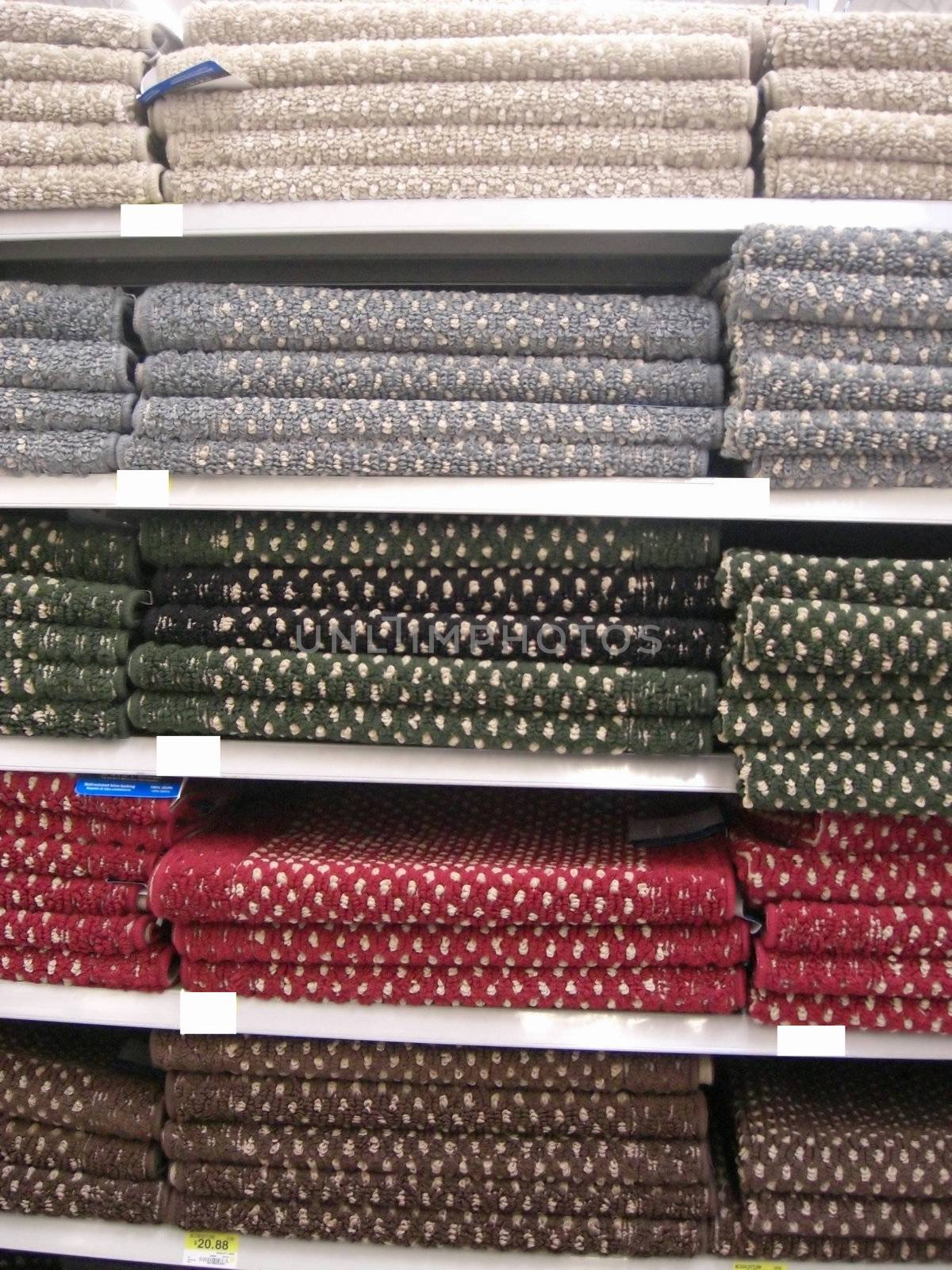 A variety of colors of bathroom rugs are neatly packed on the shelves at a retail store.