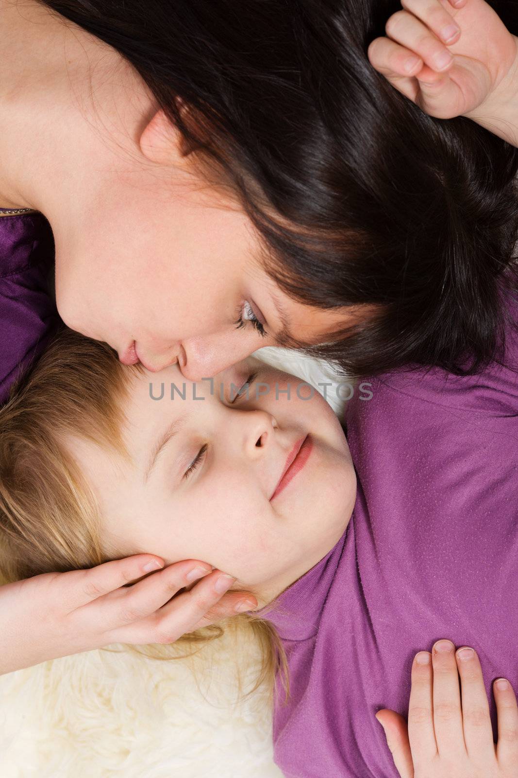 Mother kissing sleeping daughter lying heads only