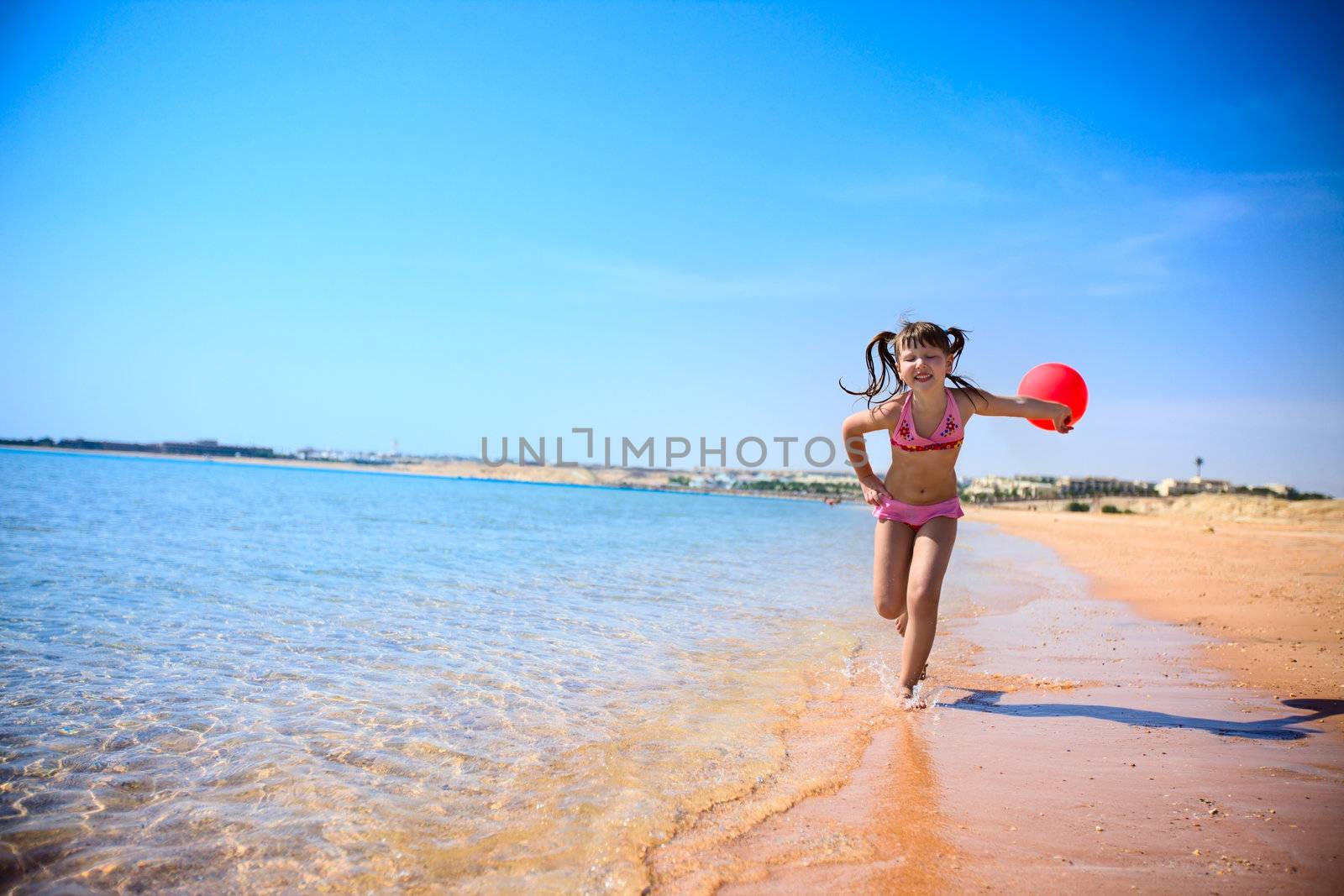 Girl Running on sunny beach with red balloon