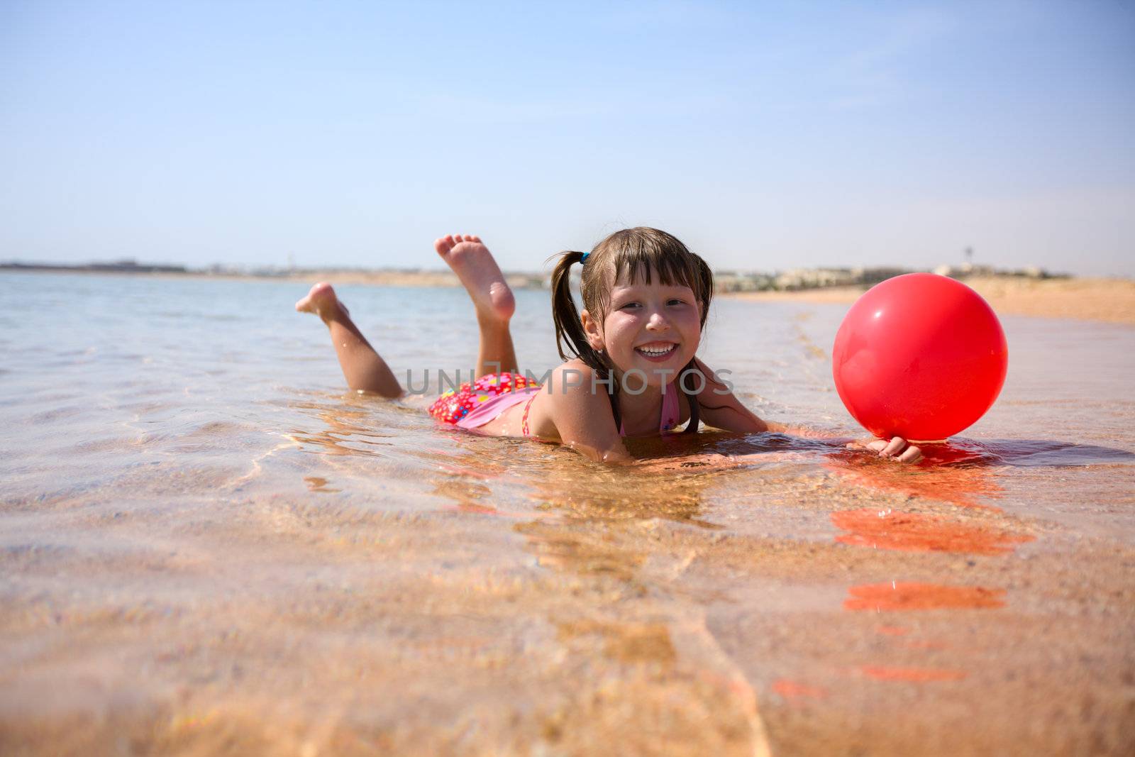 Girl on beach in water with red balloon