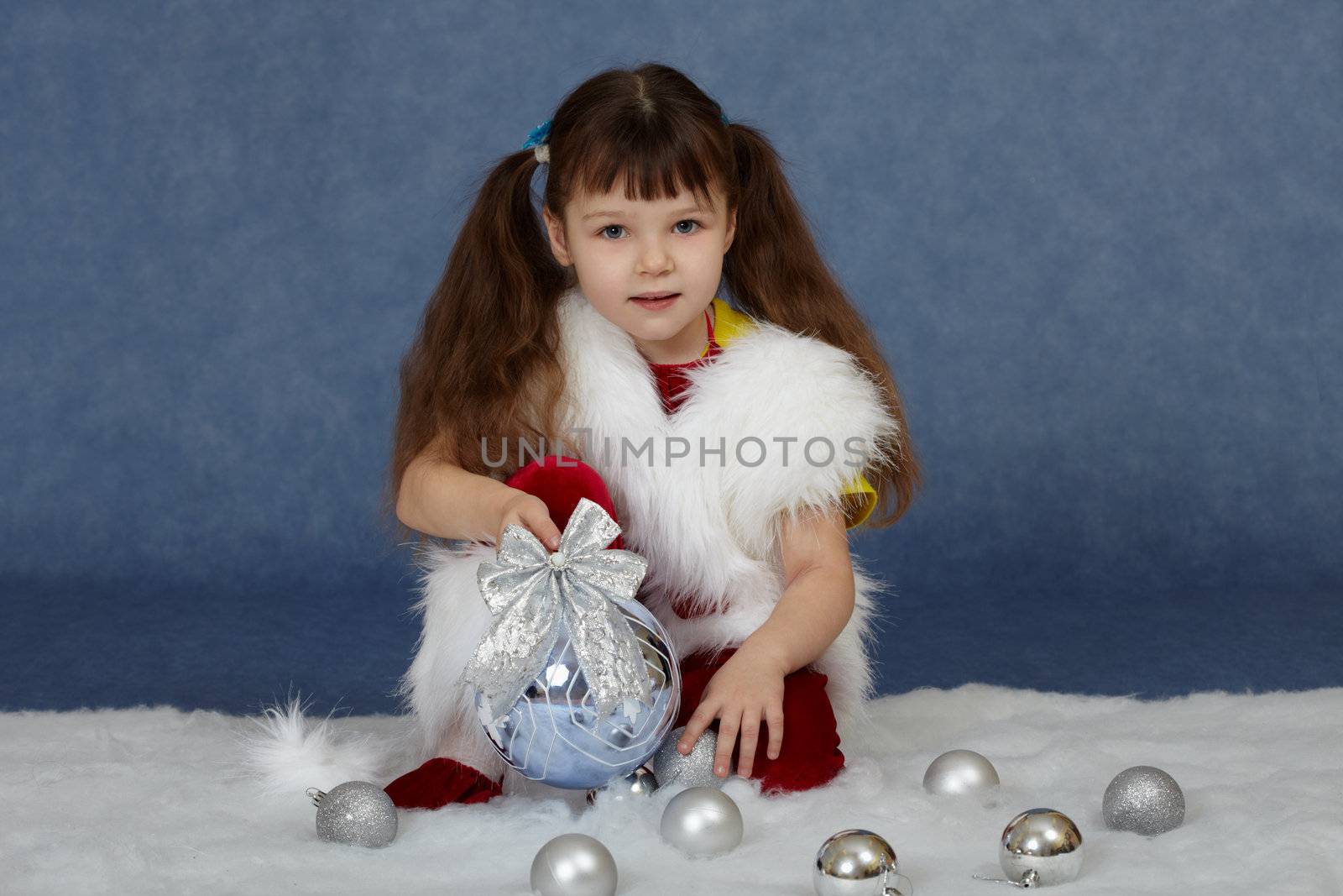 The child sits on a blue background with Christmas tree ball