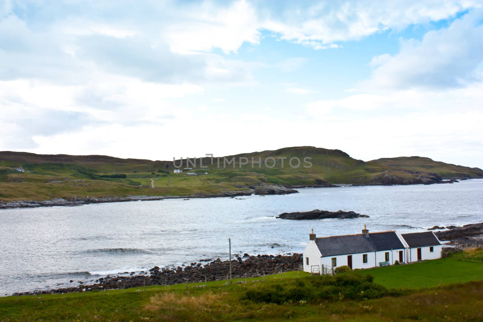 Panorama with a traditional Scottish house in front of a lake.