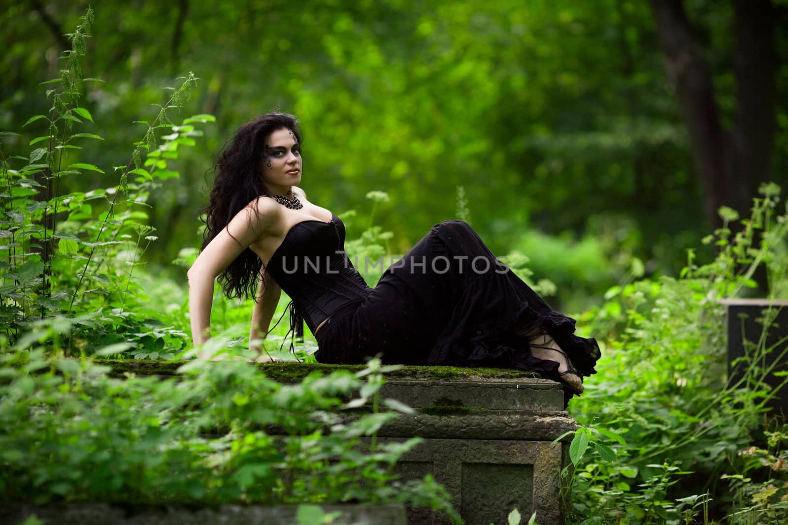 Young beautiful demonic female creature sitting on gravestone