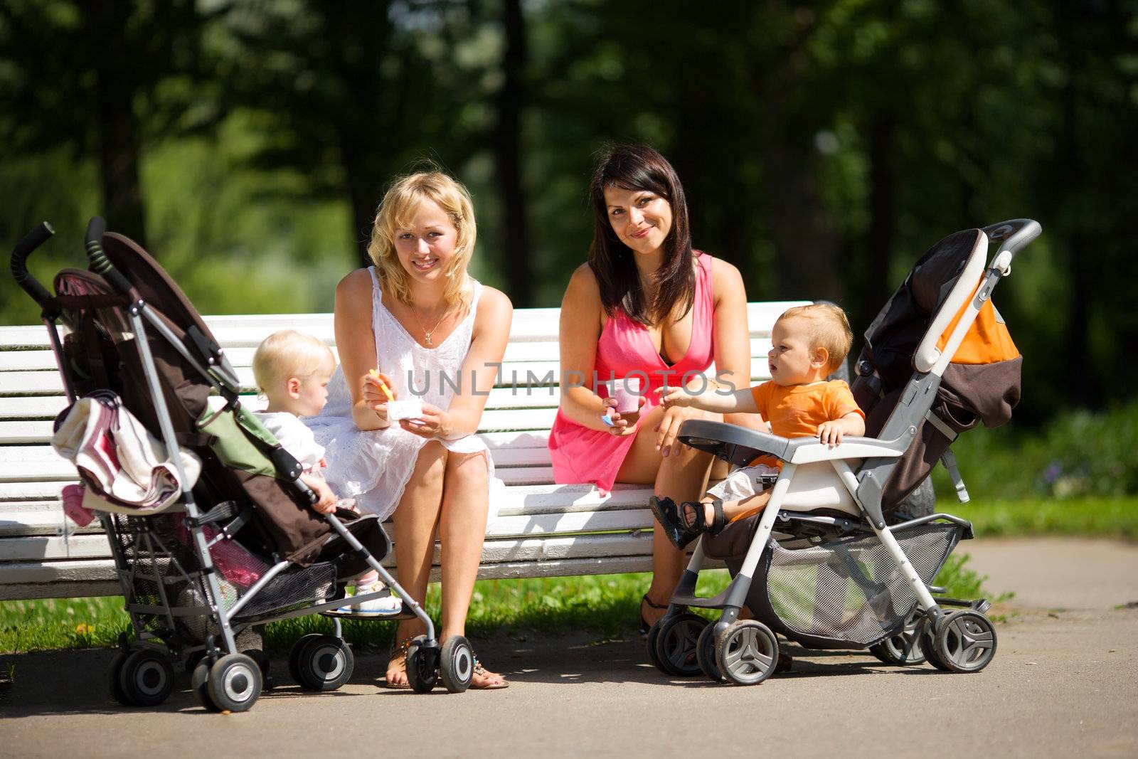 Two mothers spoon feeding their babies sitting on bench