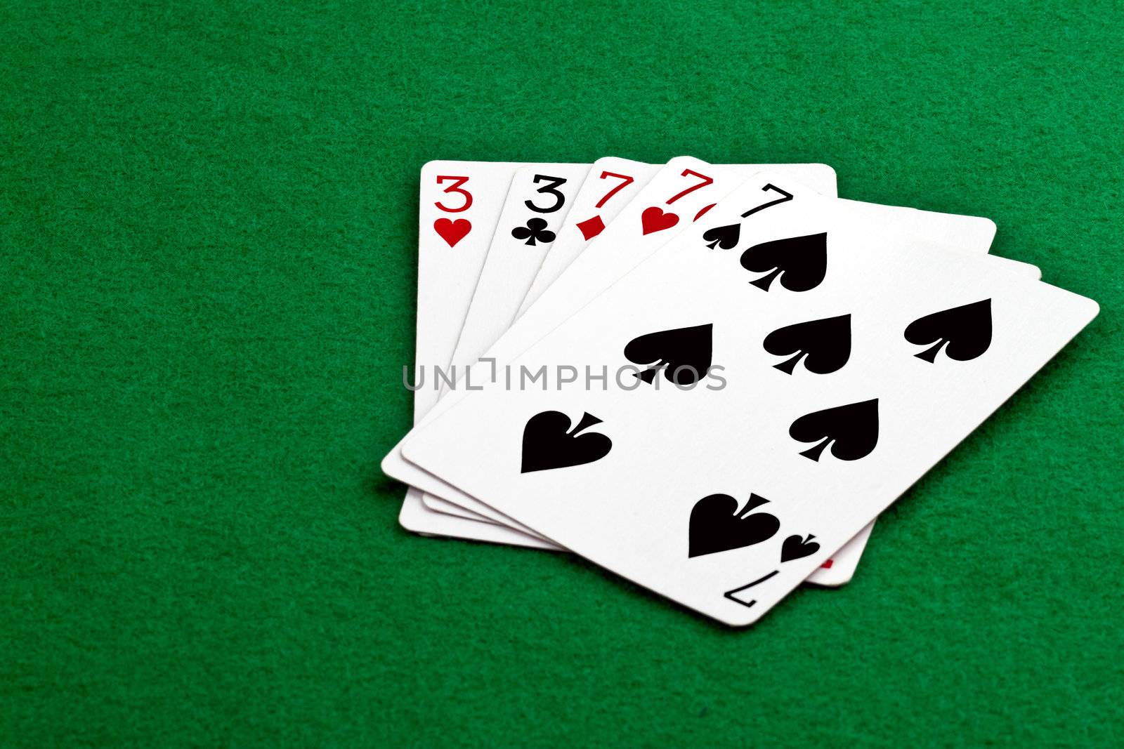 Poker hand full house with threes and sevens on green felt