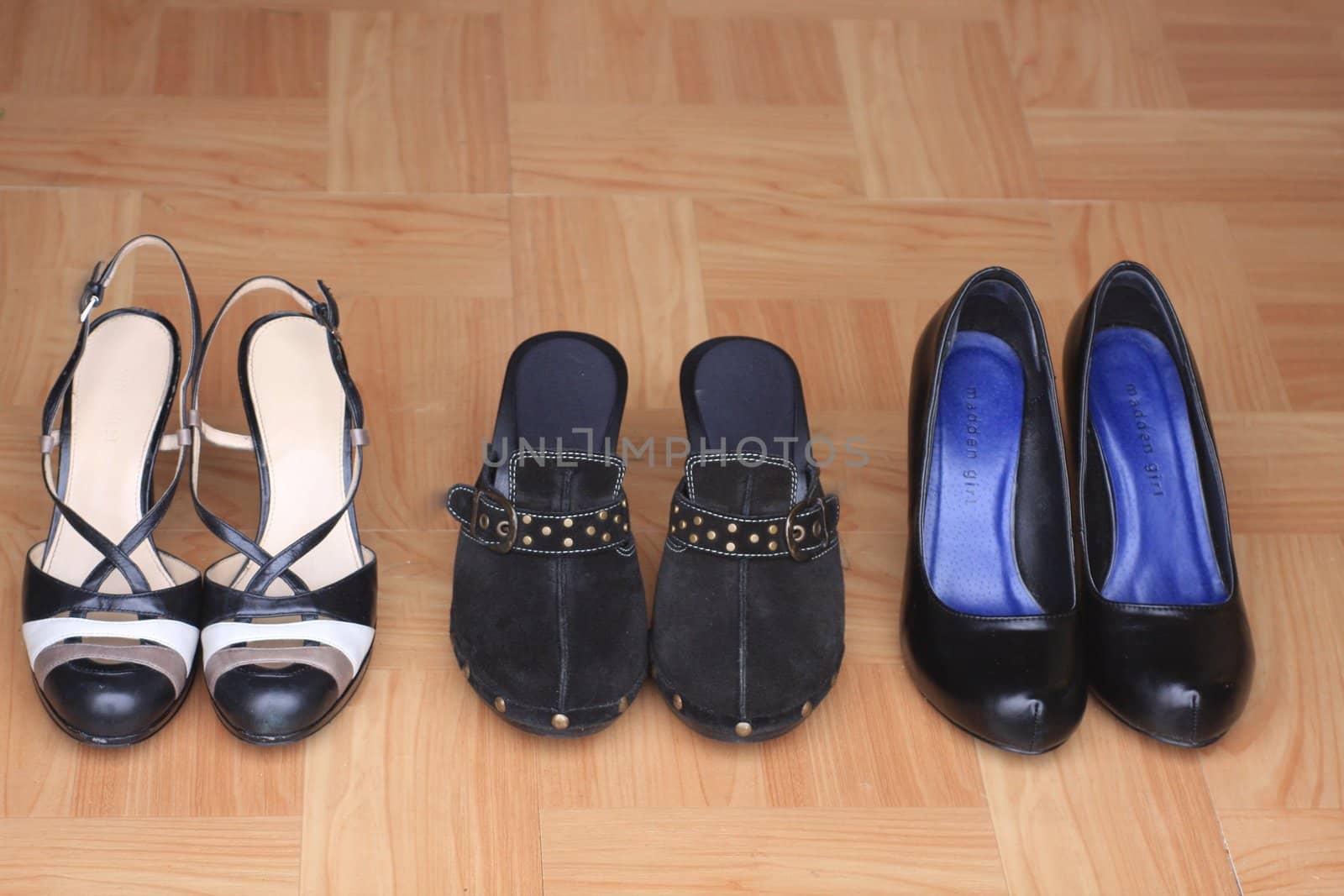 Three pairs of black women’s shoes lined up on wood floor by door. Attractive women’s foot wear for fashion, home and shopping.