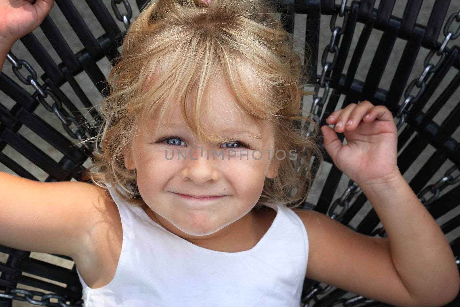 Little girl lying on a large swing, looking at the camera.