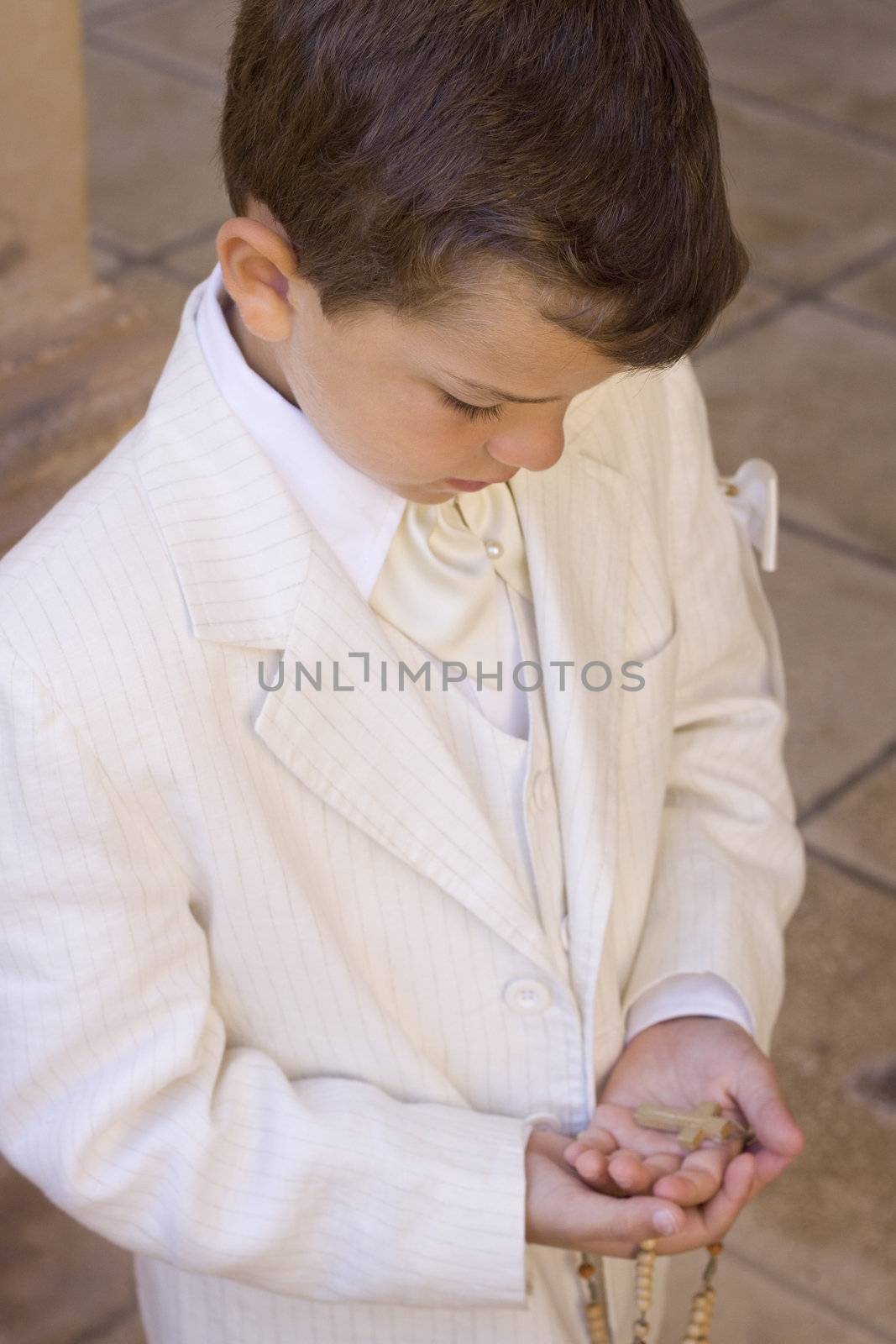 Child holding a rosary with a crucifix during his first communion celebration