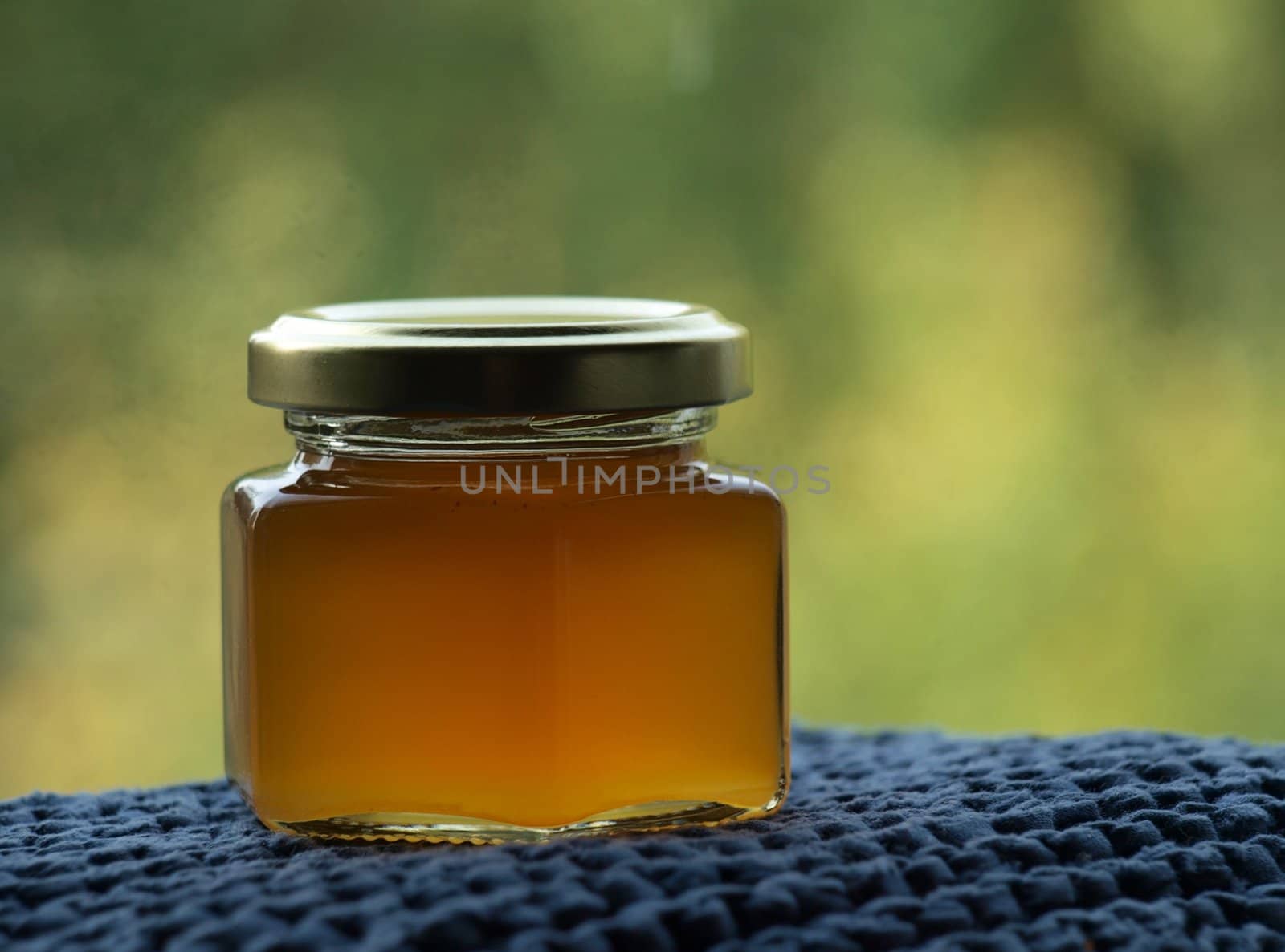 Closed jar of liquid golden honey on a blue and green background