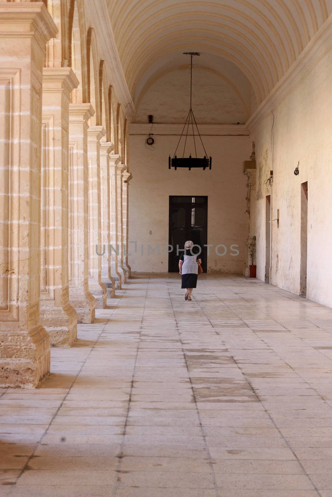 An old lady is walking through an old convent passage